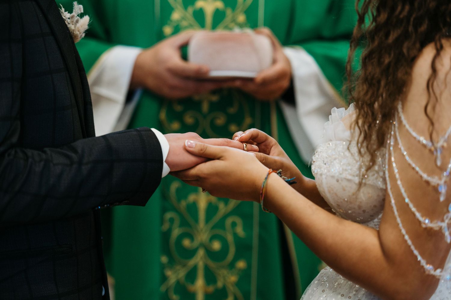 A close-up shot of hands exchanging wedding rings during a ceremony against a green backdrop.