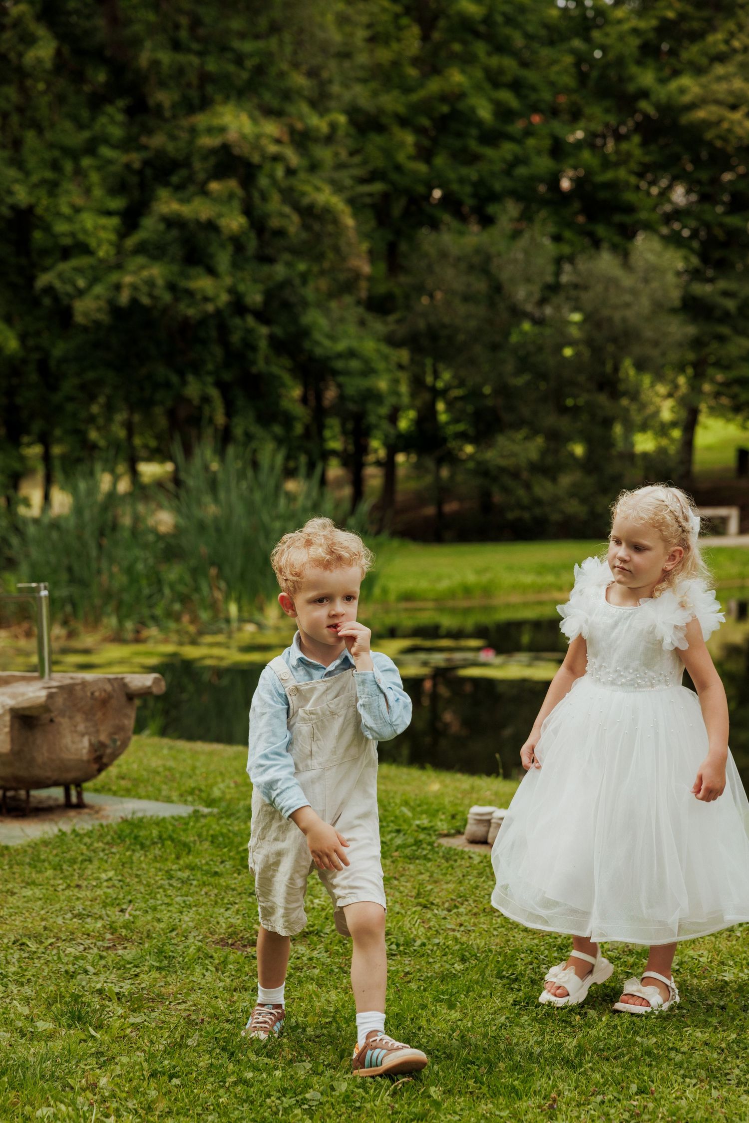 Children playing and running on green grass in formal white outfits.