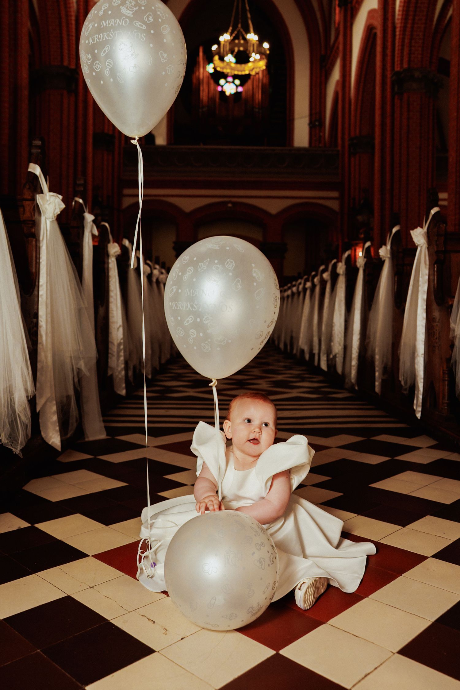 White balloons float in an elegant church aisle with checkered floor and red curtains.