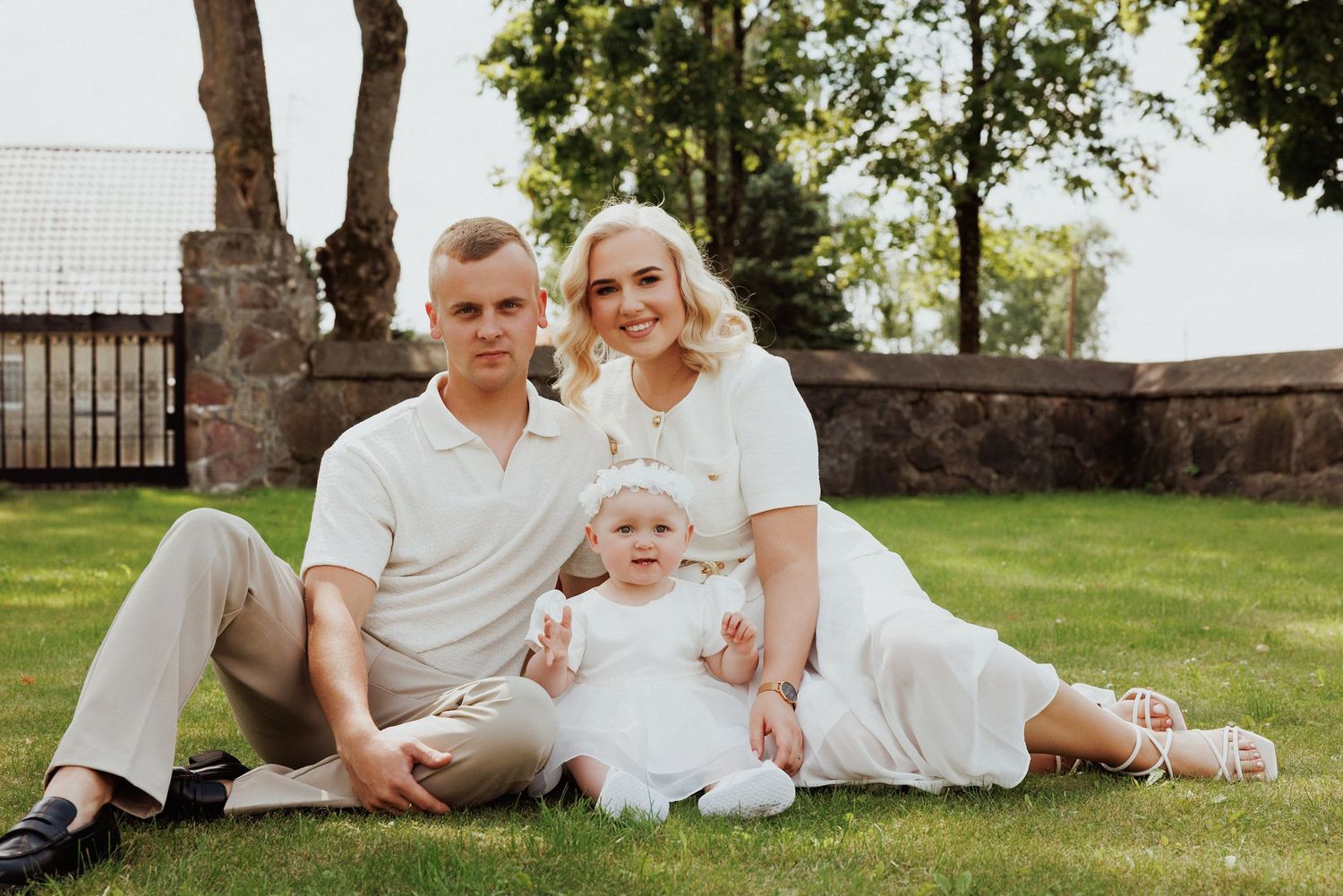A family dressed in white sits together on grass in a sunny outdoor setting.