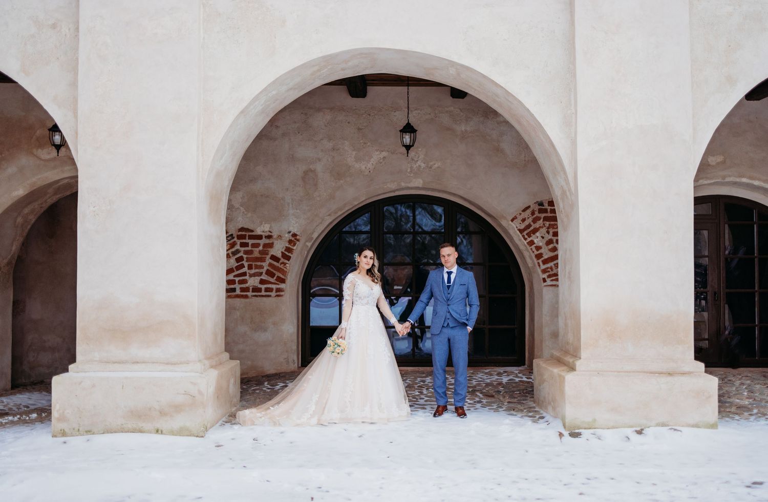 Elegant wedding portrait under arched colonnade with exposed brick and stone details.