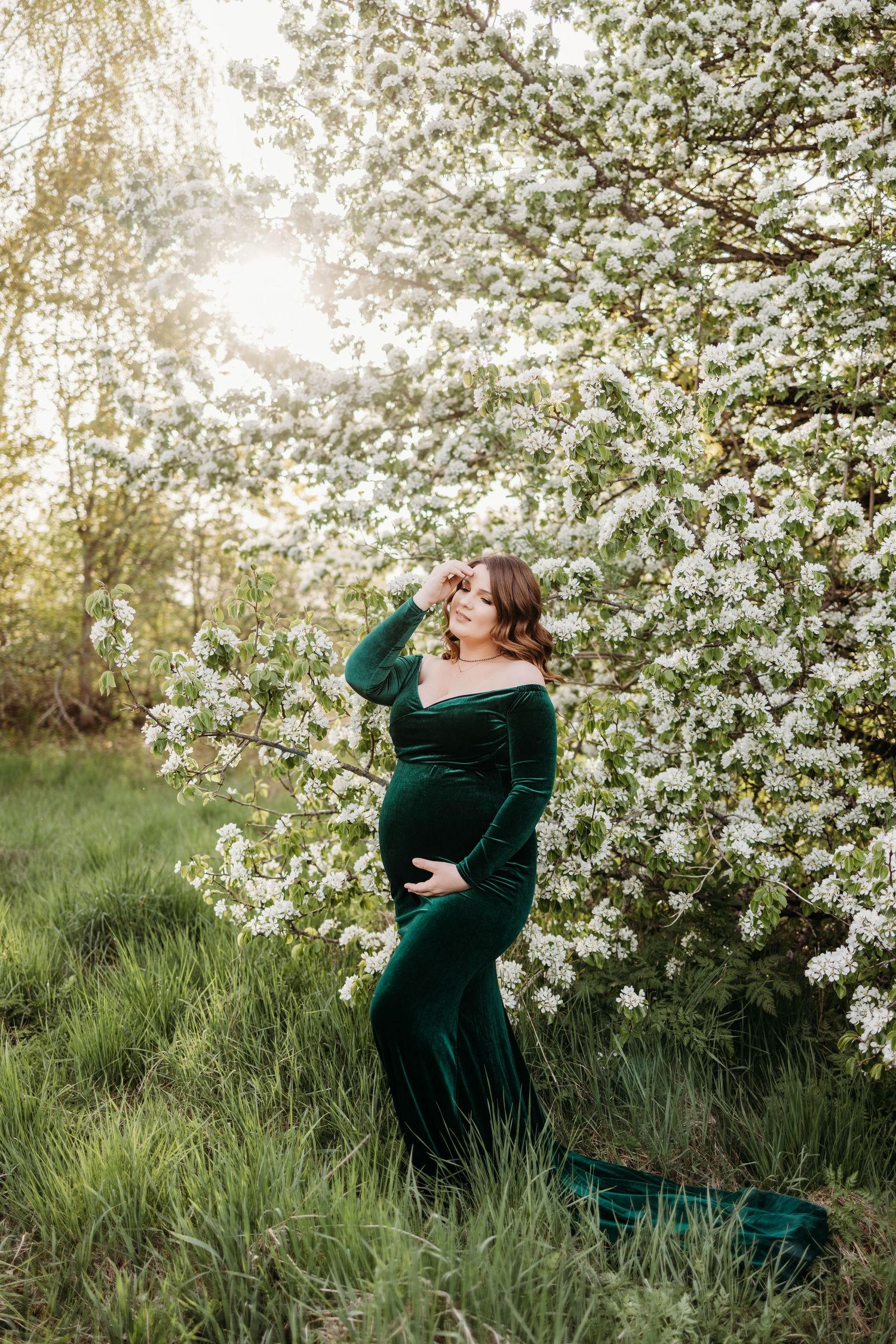 Elegant maternity portraits in emerald velvet against flowering spring trees at sunset.