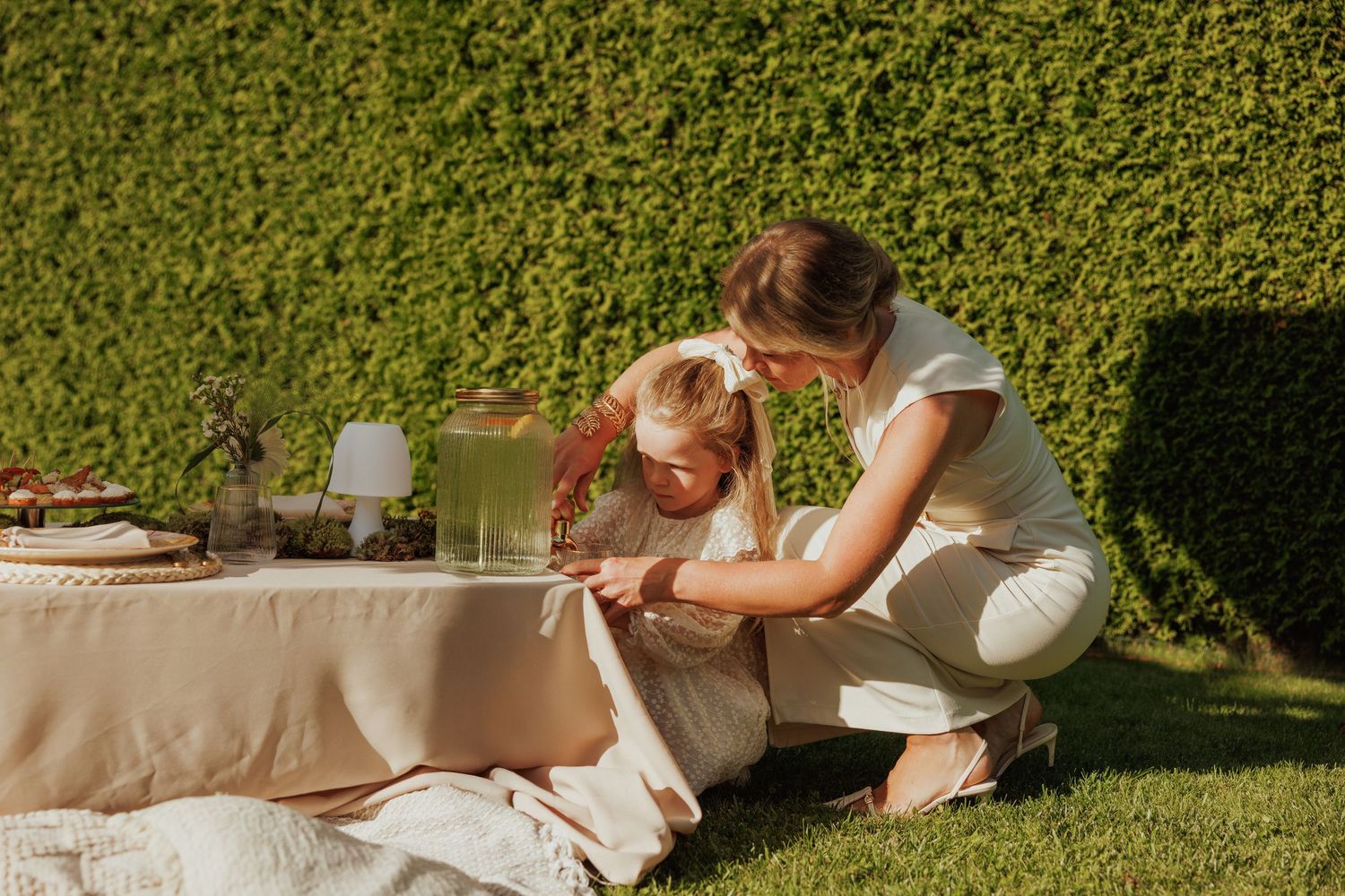 Outdoor garden party setup with beige tablecloth and lush hedge background.