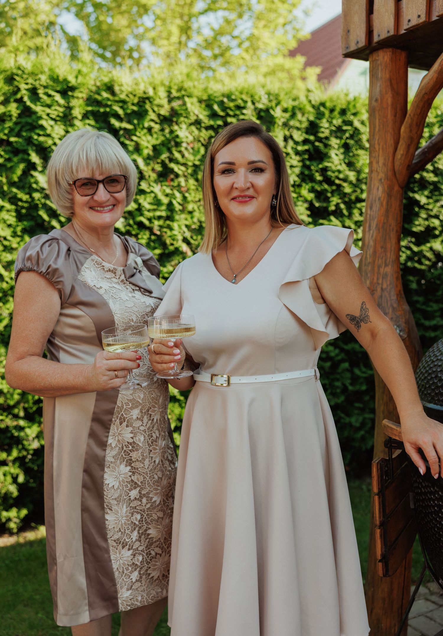 Group wearing coordinated neutral dresses toast with drinks at outdoor celebration.