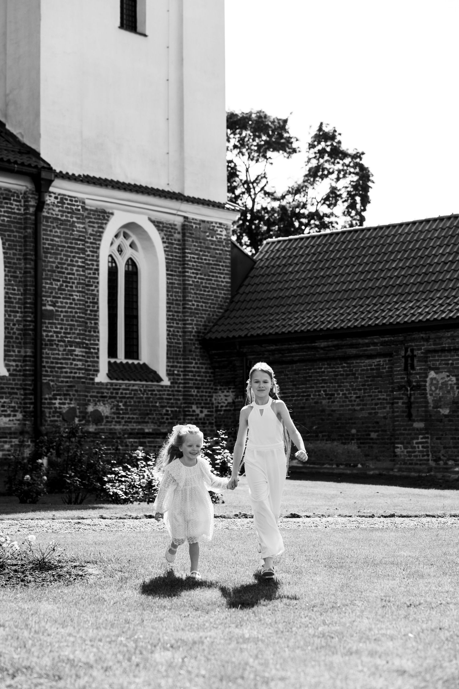 Black and white photo of people in white dresses walking near a church building.
