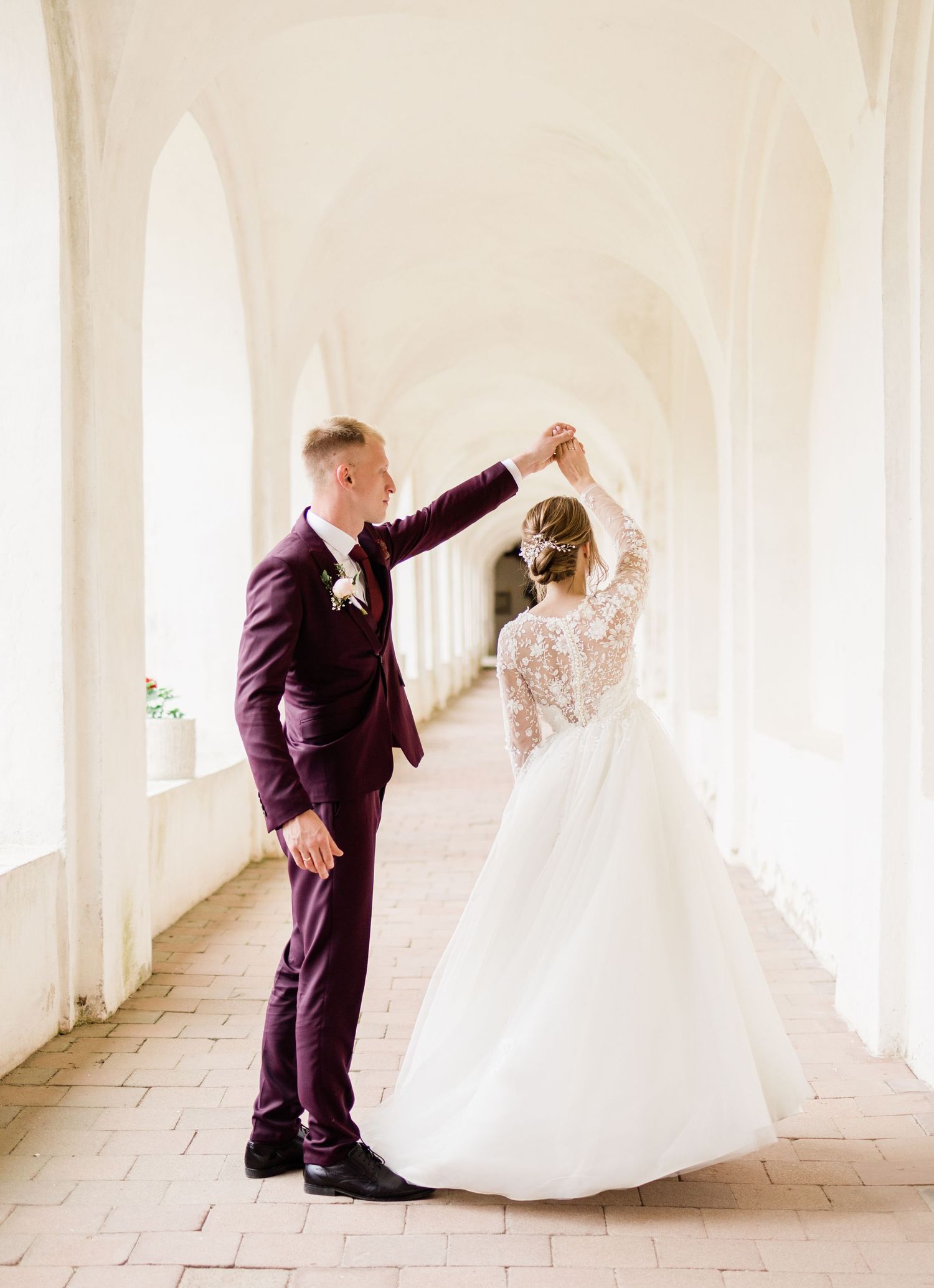 Wedding couple dances and twirls in sunlit white colonnade.