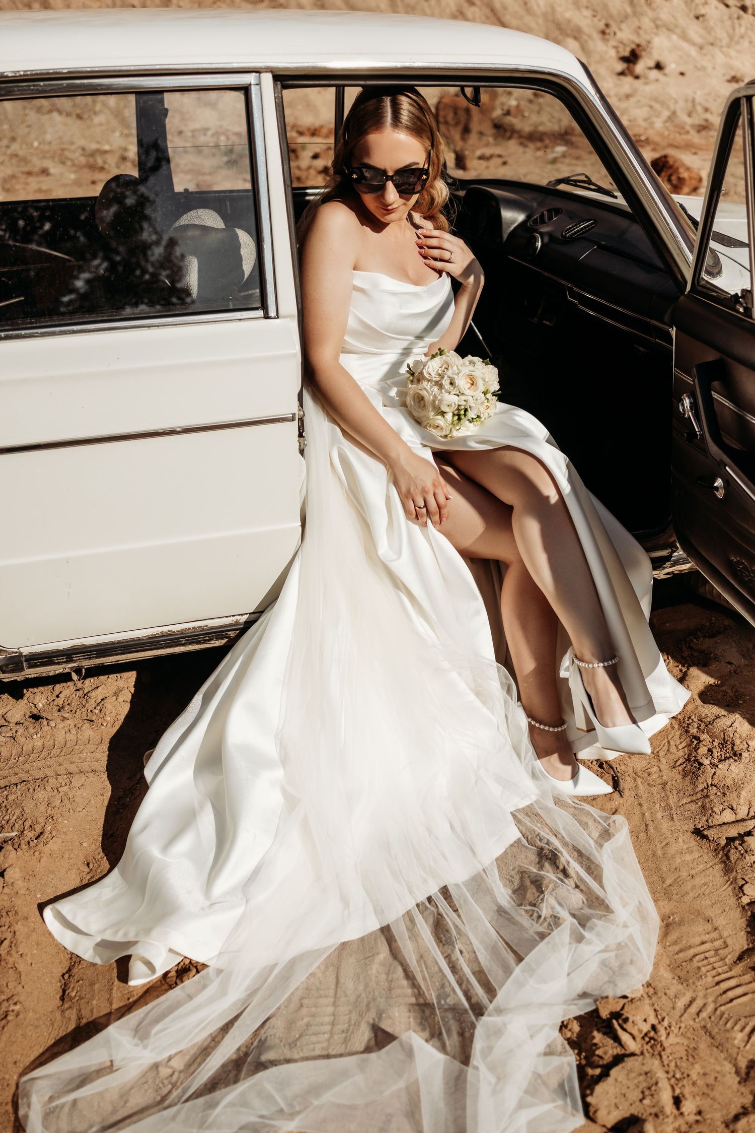 A classic white vintage car serves as an elegant backdrop for wedding photography in a desert setting.