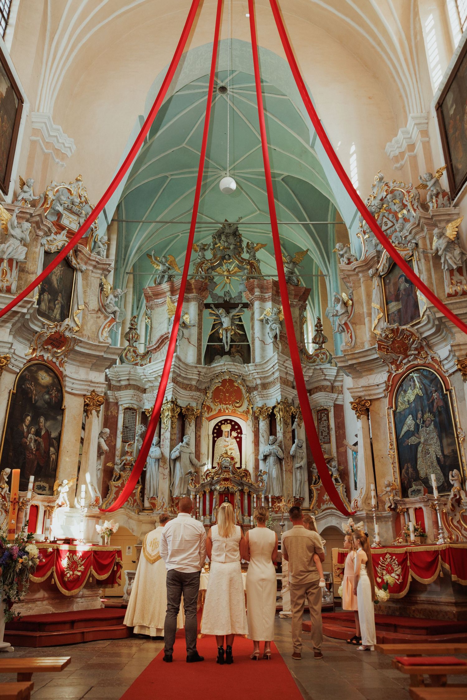 Interior of an ornate baroque church with red draping and decorative altar during a wedding ceremony.
