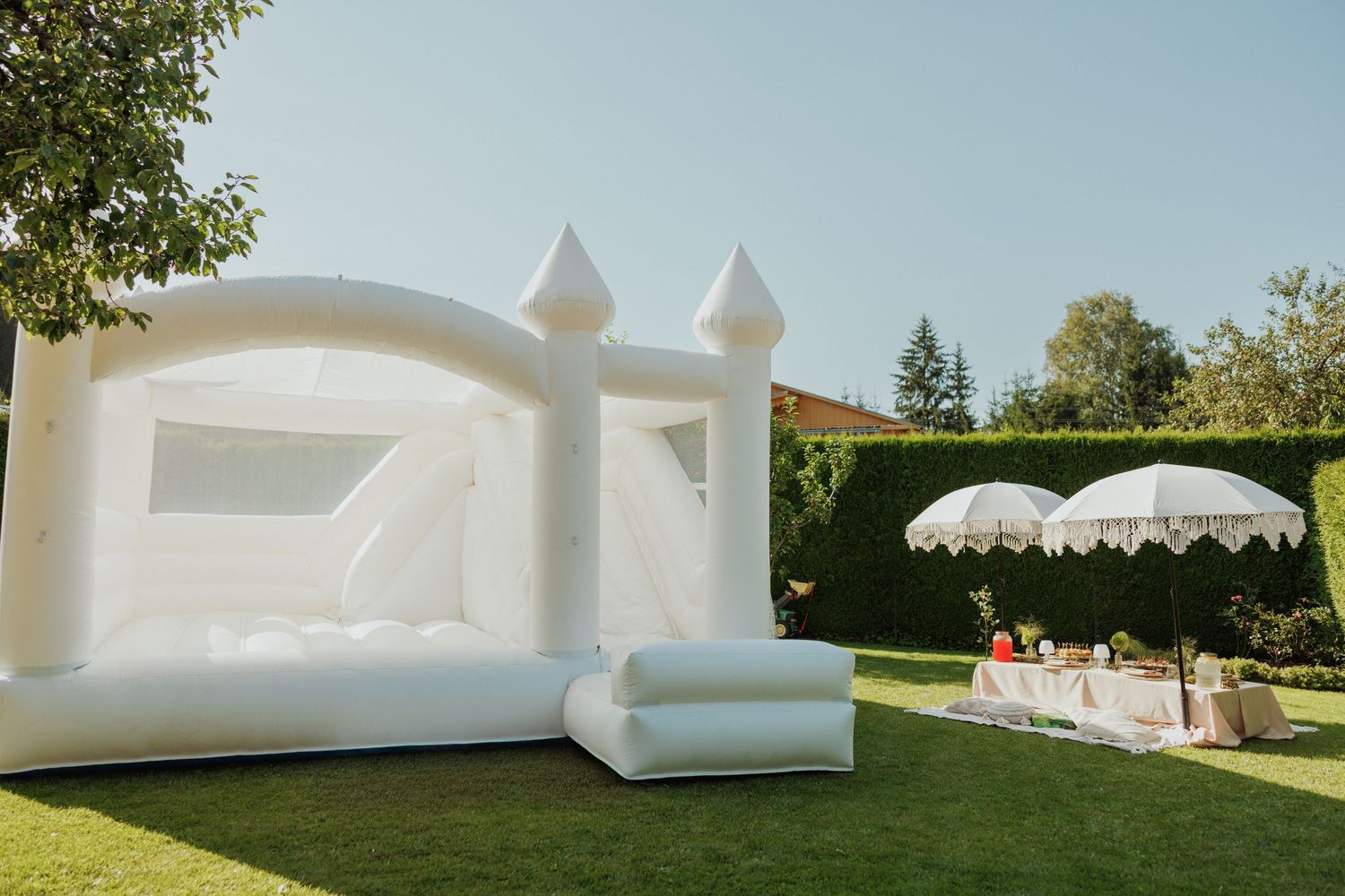 White inflatable bounce house castle set up on a lawn with a decorative umbrella in the background.