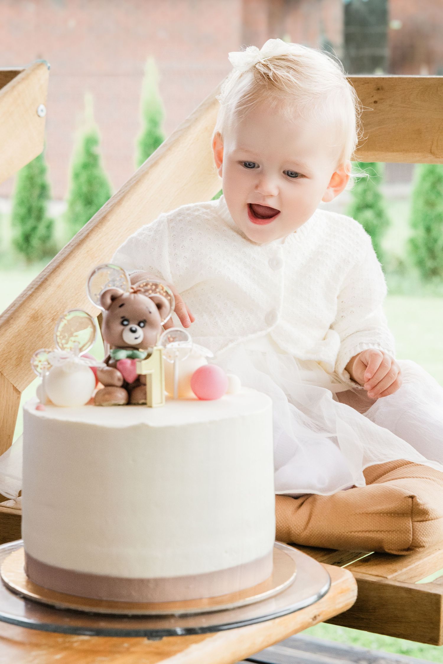 White birthday cake with a small teddy bear topper displayed on a wooden surface.