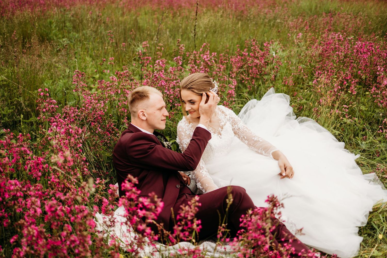 Romantic wedding couple sitting among vibrant pink wildflowers in a meadow.