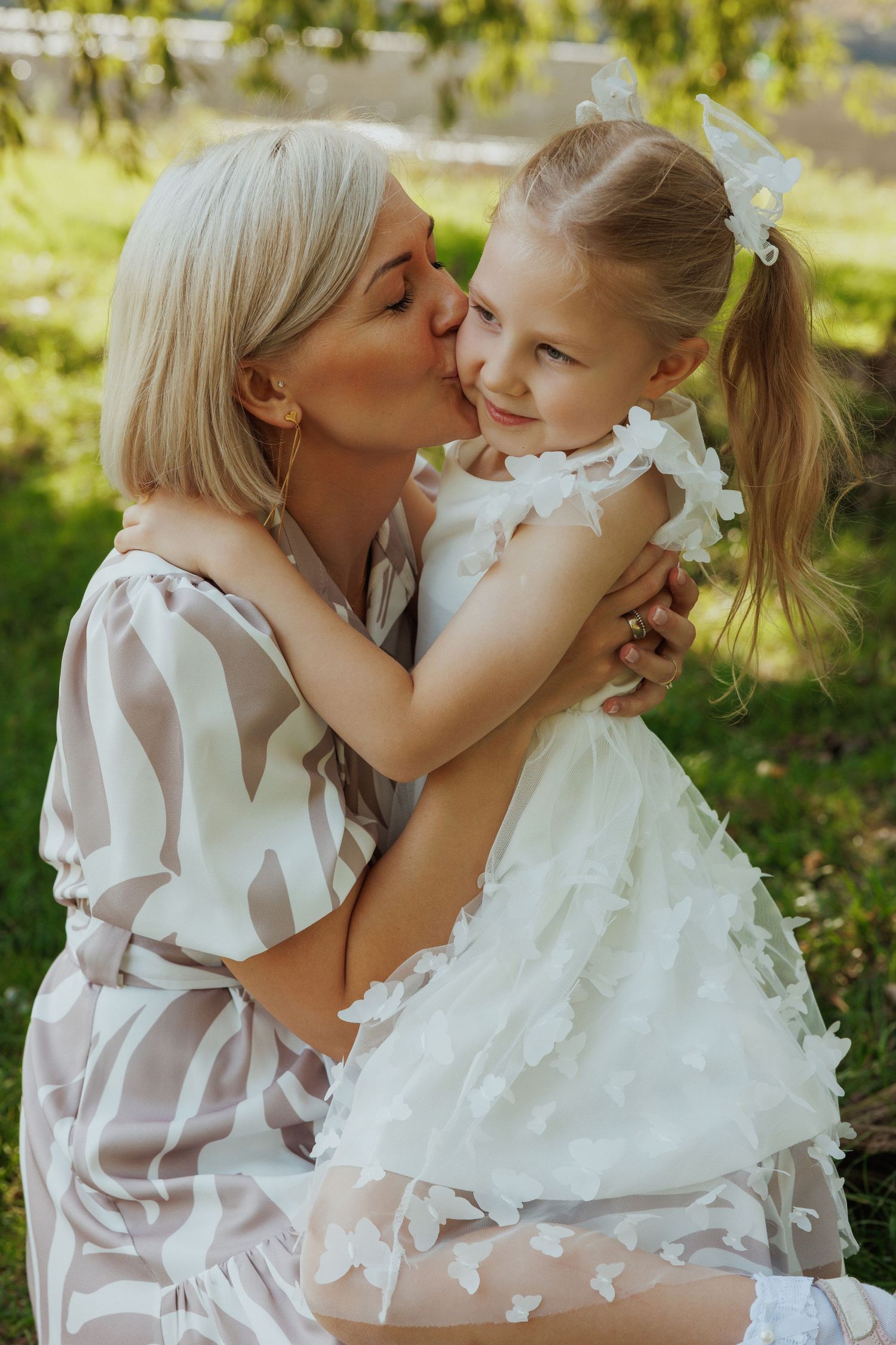 A tender moment shared between two people in white dresses against a sunlit garden background.