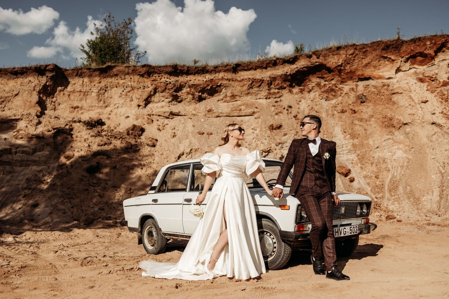 Panoramic wedding photo shoot against dramatic desert cliffs with vintage car.