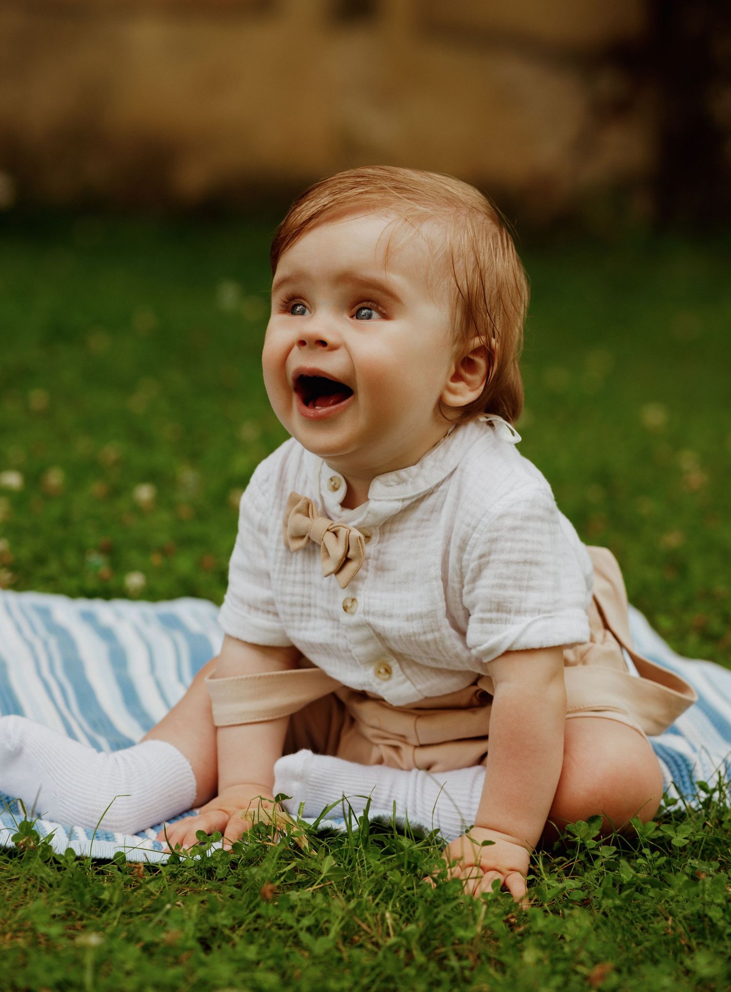 Baby in white clothing crawls and plays on green grass during a sunny outdoor photo session.
