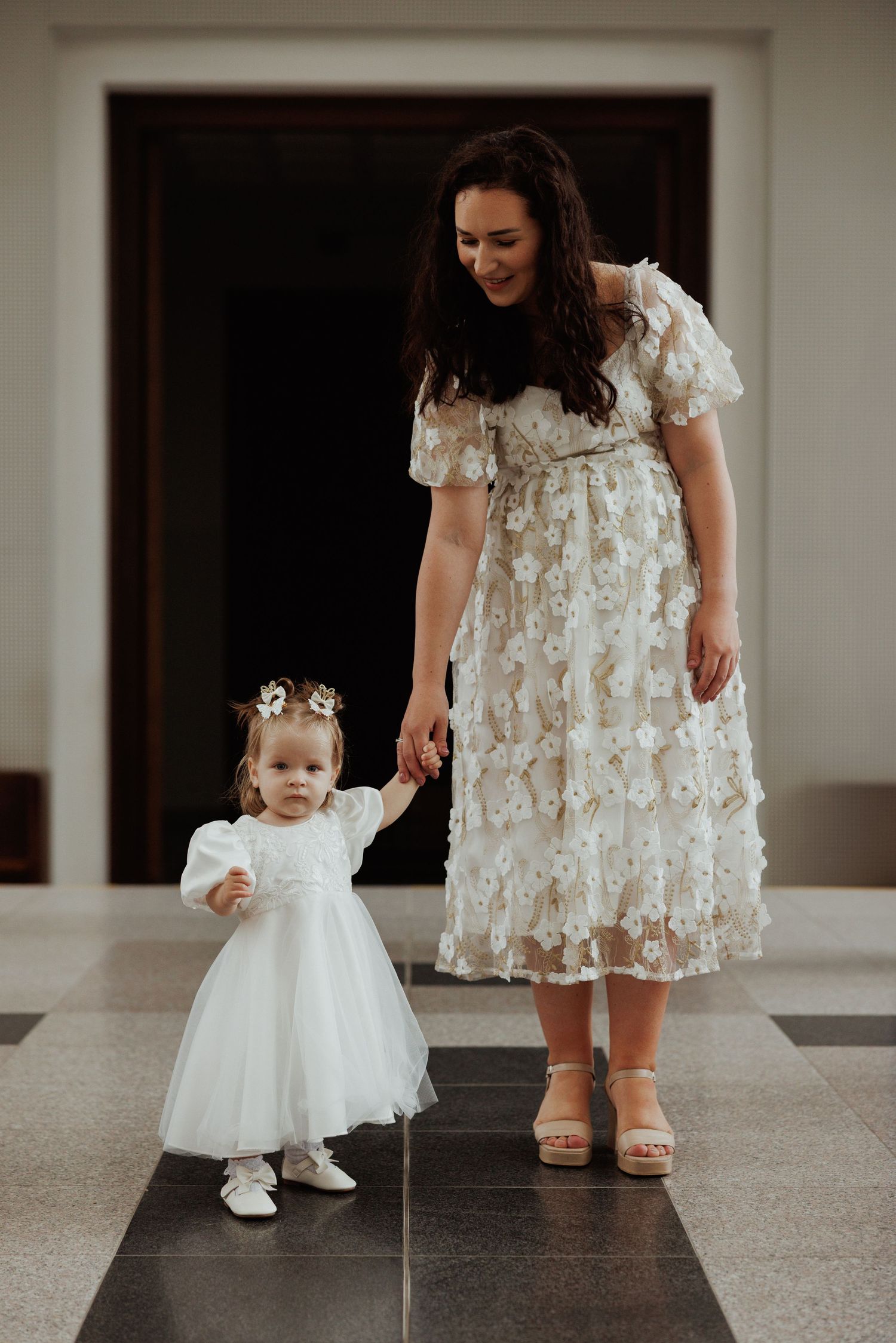 Heartwarming sequence showing tender interactions between adults and a toddler wearing matching white dresses.