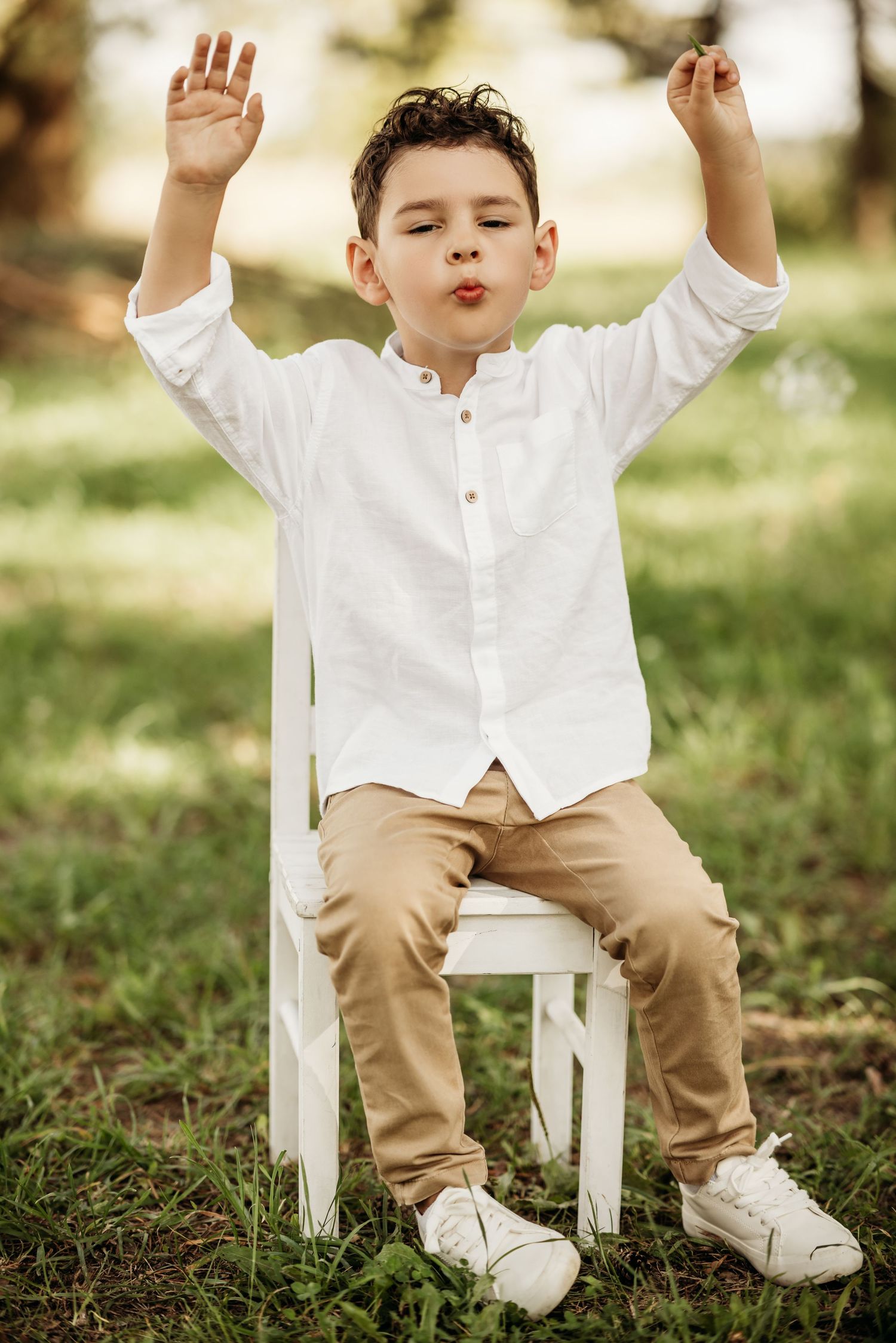 A playful scene outdoors with a white chair, featuring casual attire and raised arms in a joyful pose.