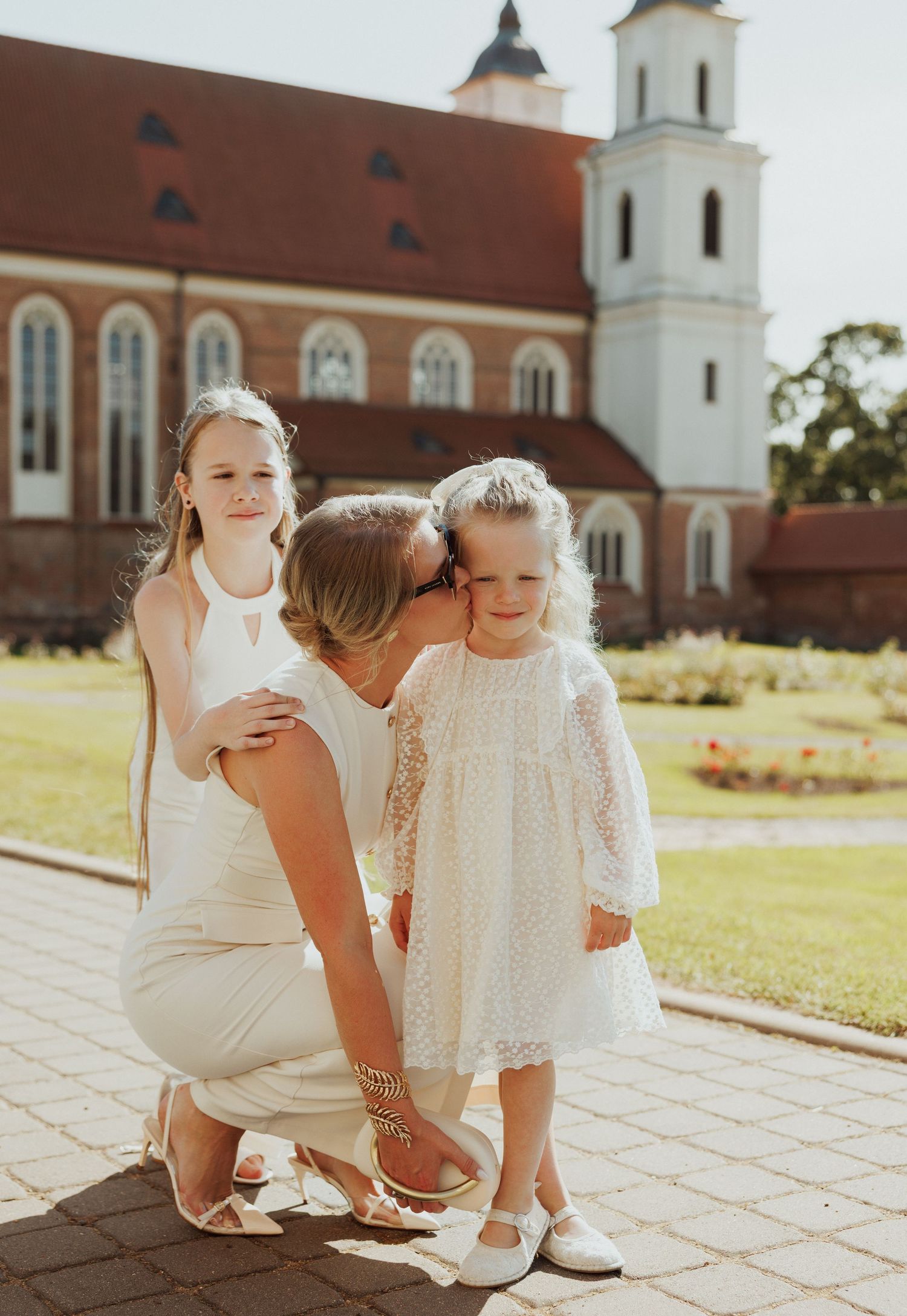 Young children in white outfits sit together on stone steps with a church building in the background.