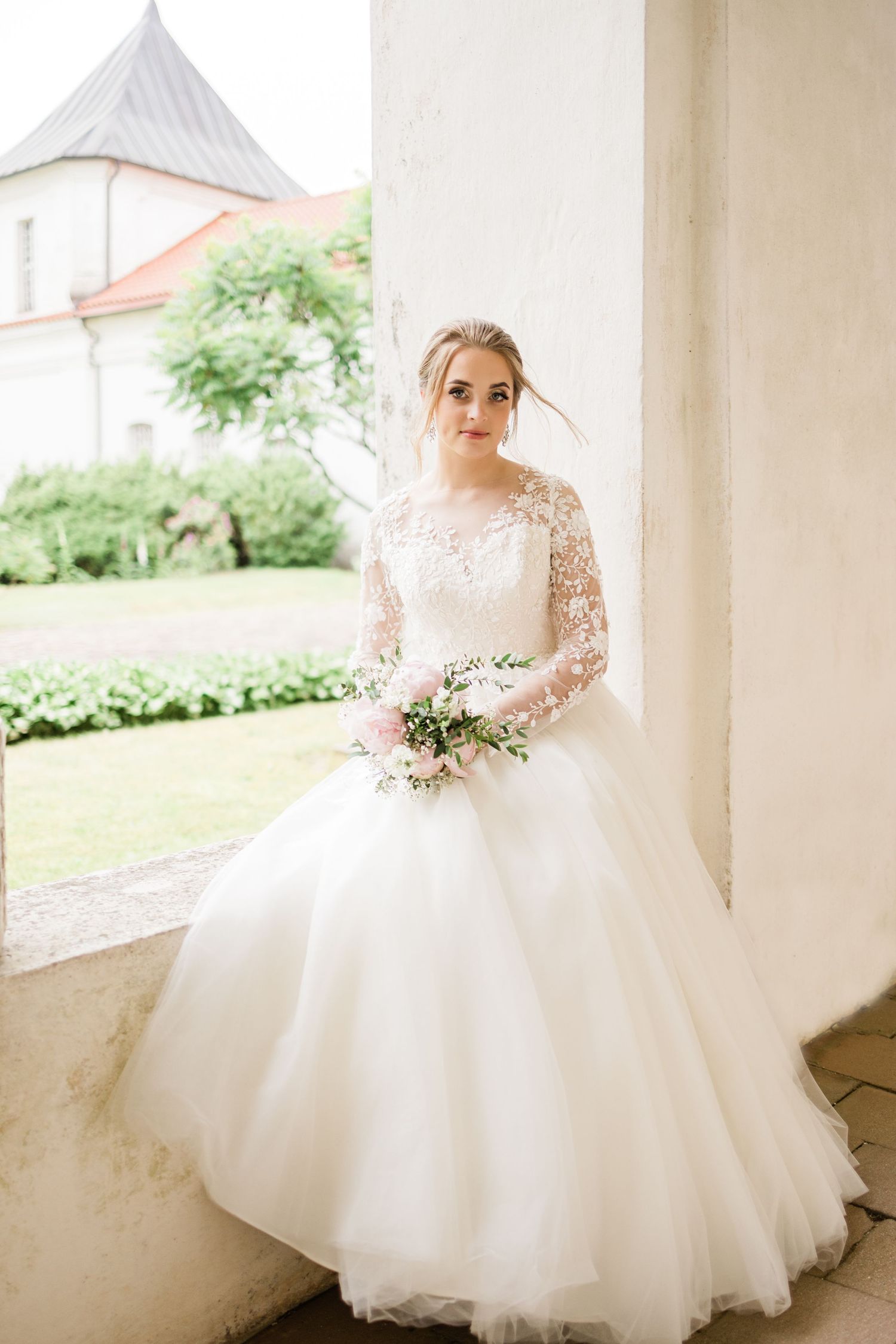 Classic bridal portrait featuring full tulle ballgown with lace sleeves against white columns.