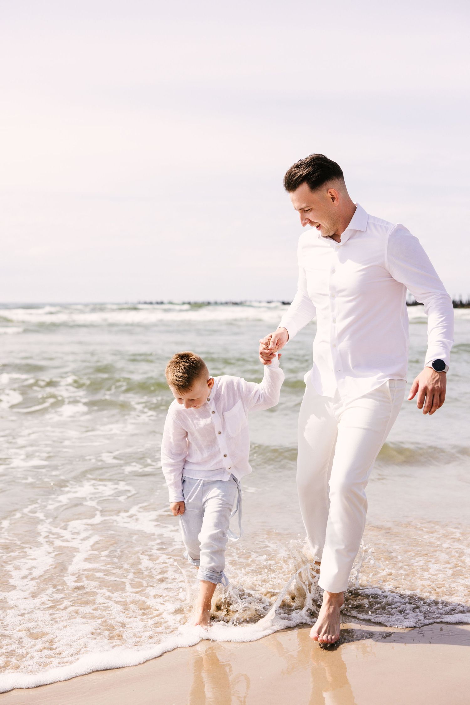 Family enjoying a playful moment together at the beach's edge wearing all white outfits.