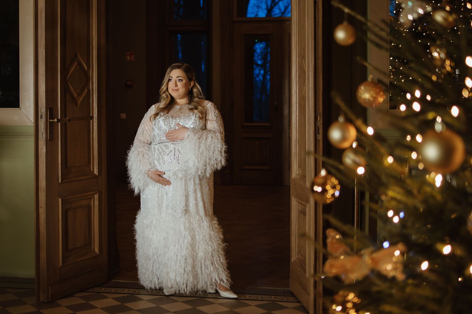Romantic wedding portrait in front of decorated Christmas trees with warm glowing lights.