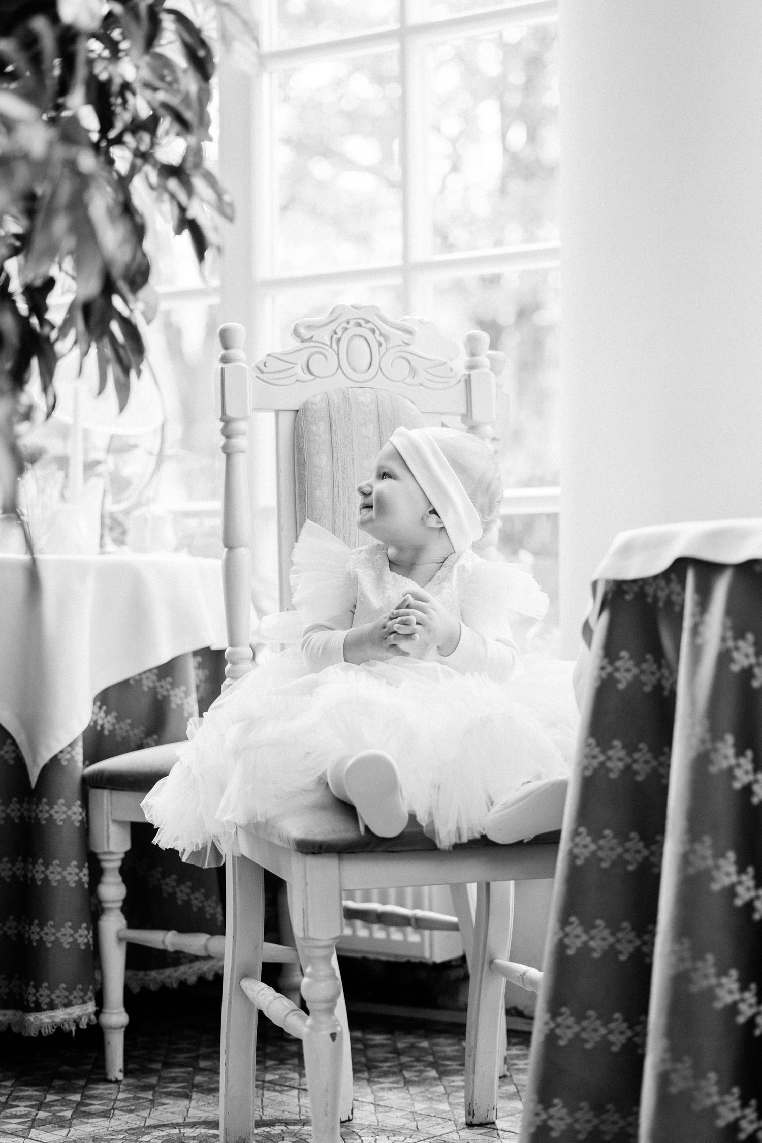 Black and white artistic photo of a dancer in a tulle skirt resting gracefully on an ornate white chair.