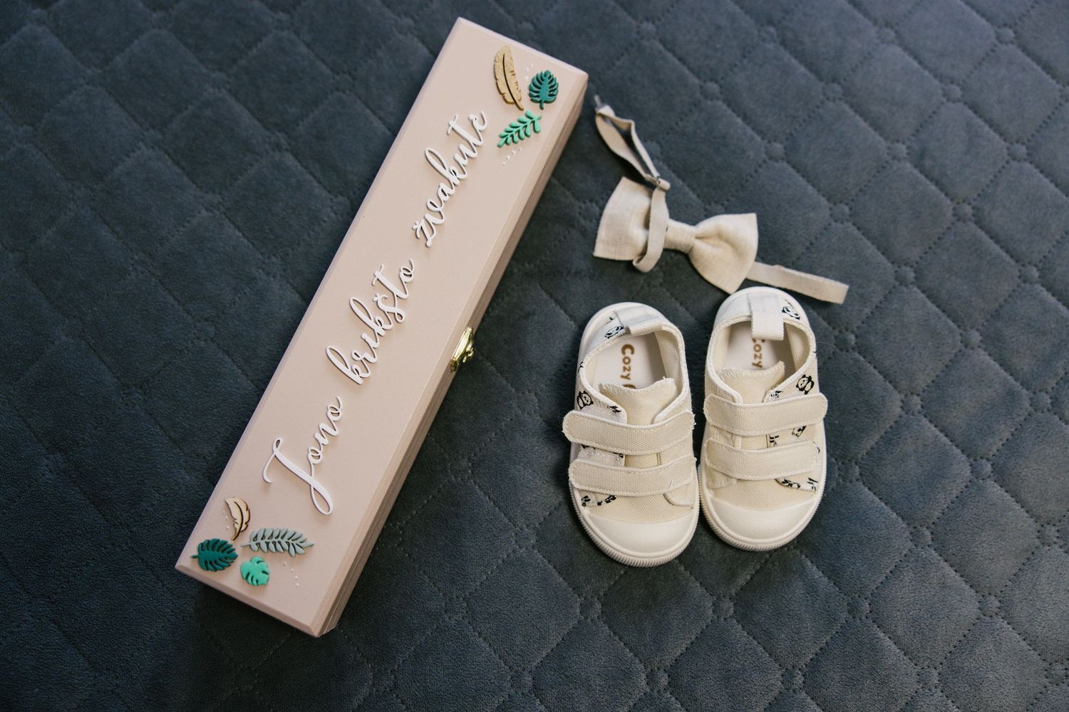 A collage of baby shoes and accessories in neutral beige and white tones arranged against a dark textured background.