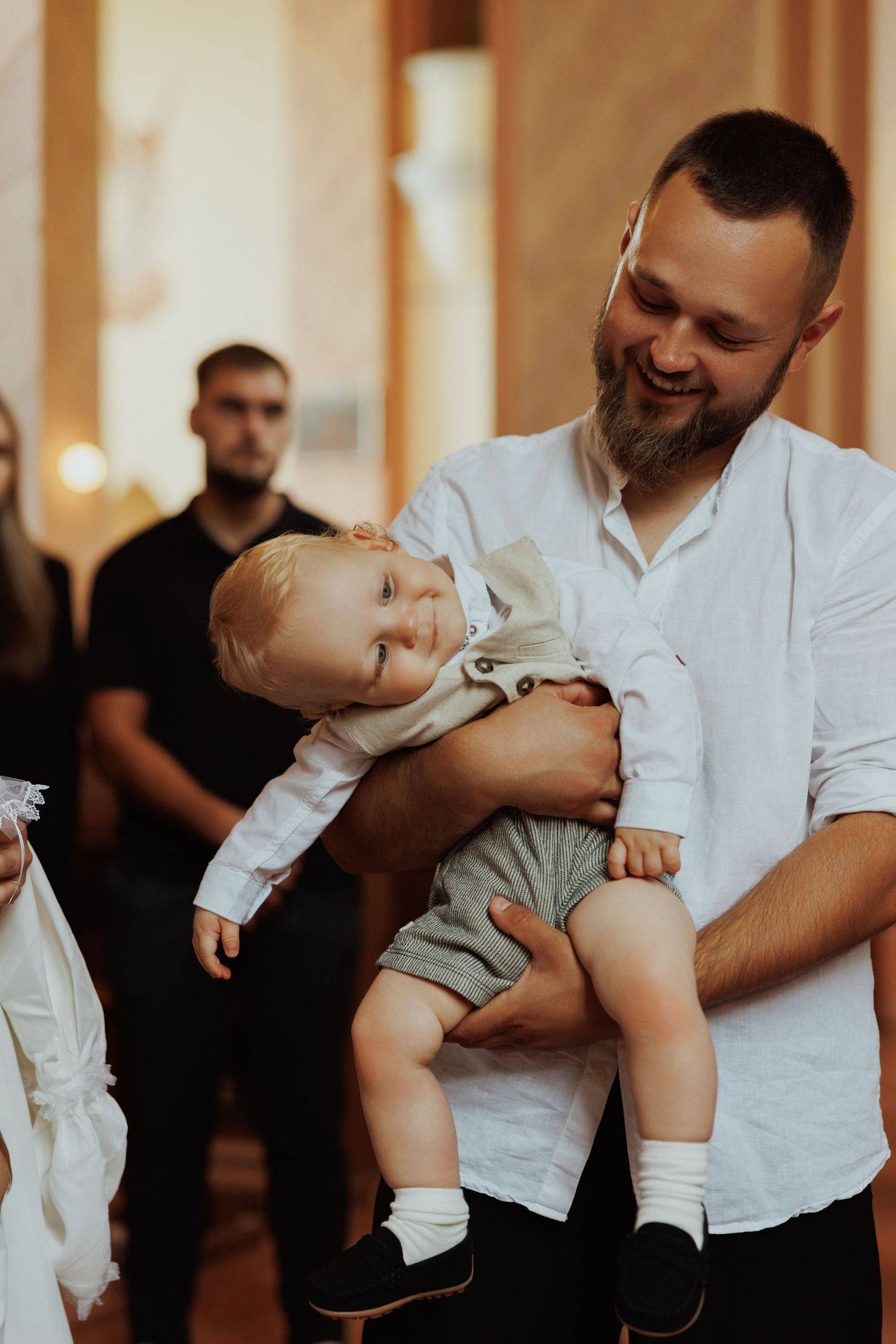 A tender moment during a baptism ceremony as a baby is held in white ceremonial clothing.