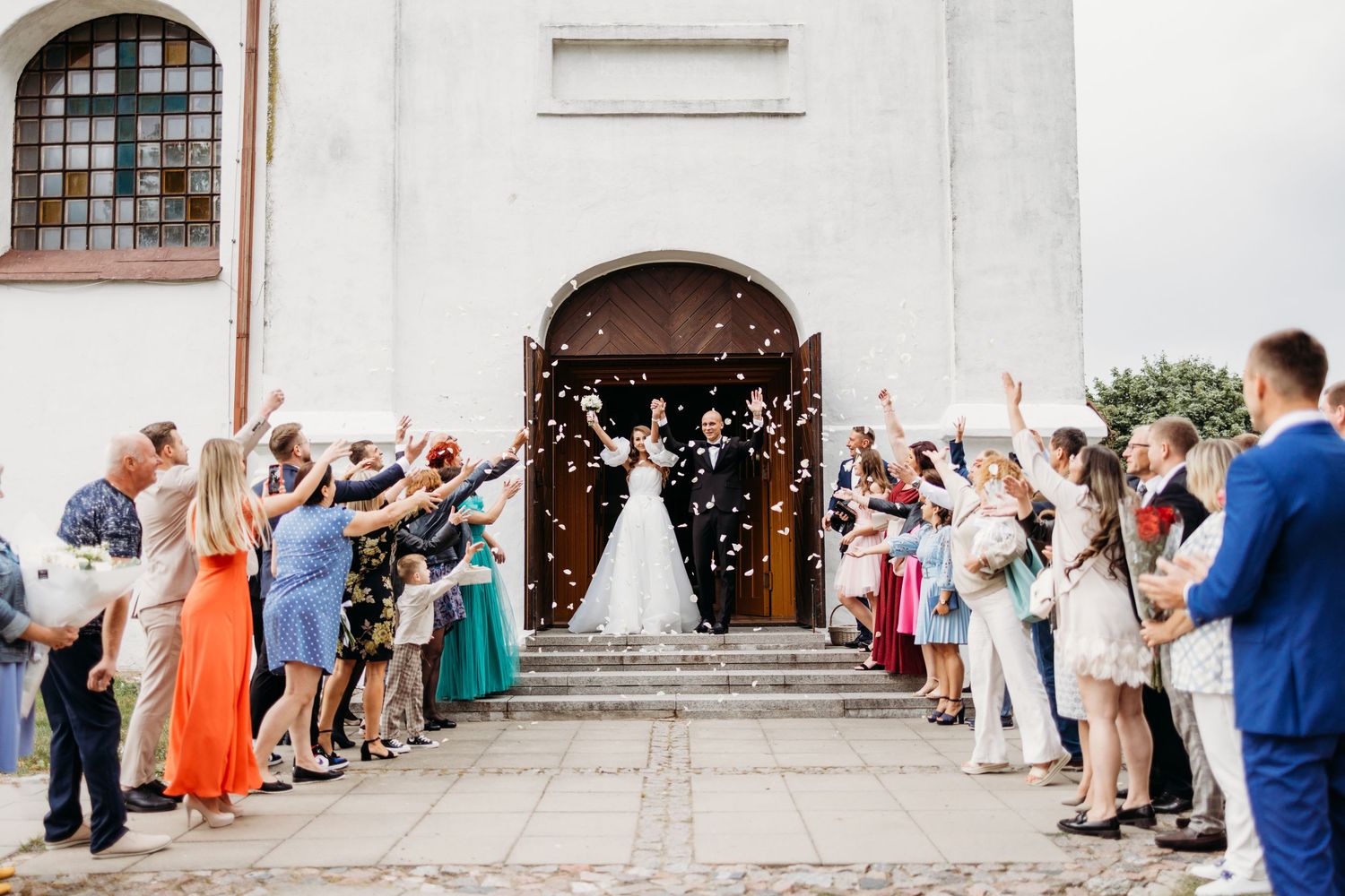 Wedding guests line up outside white church building creating celebratory exit pathway.