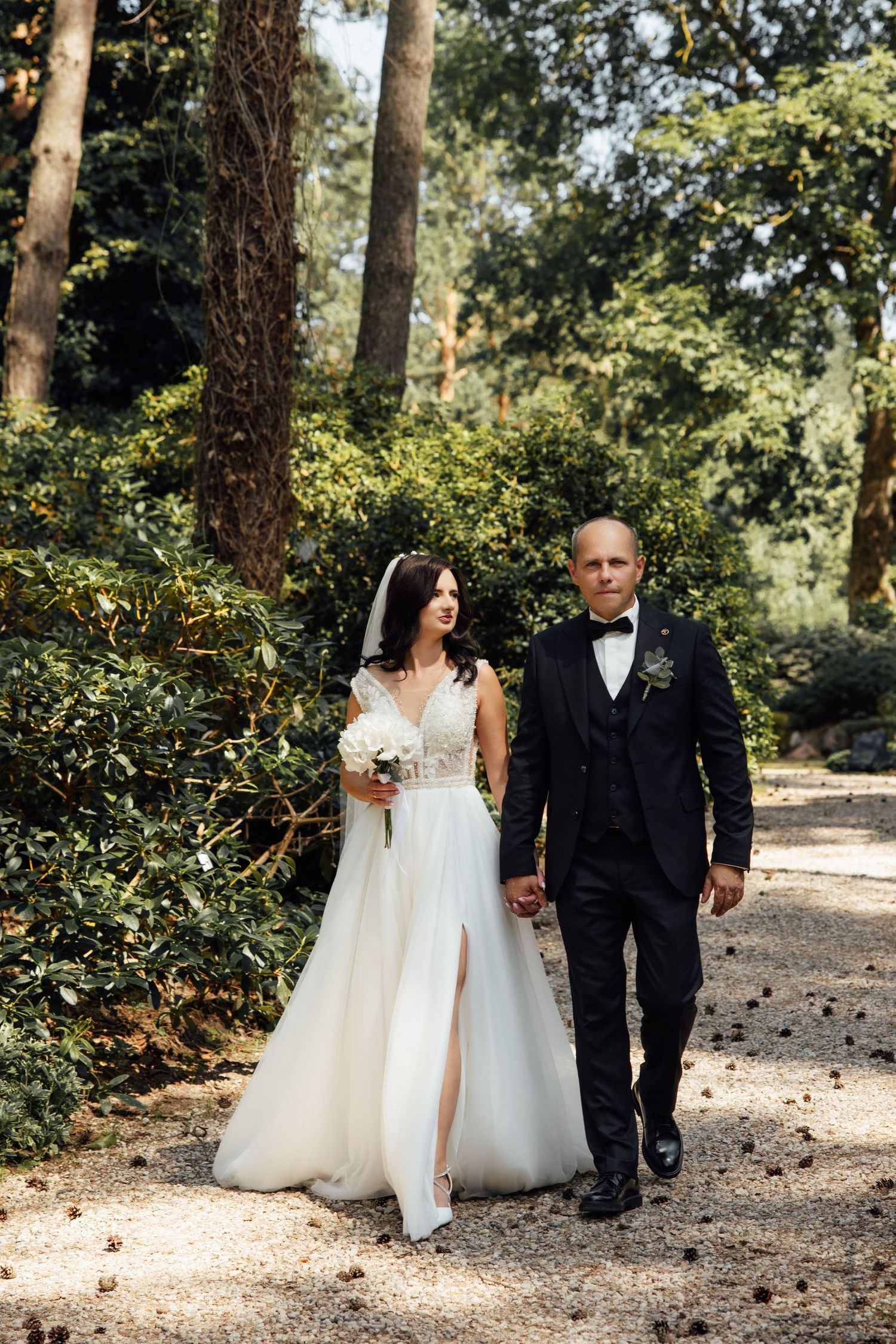 Bride and groom walking hand in hand through a lush green garden path on their wedding day.