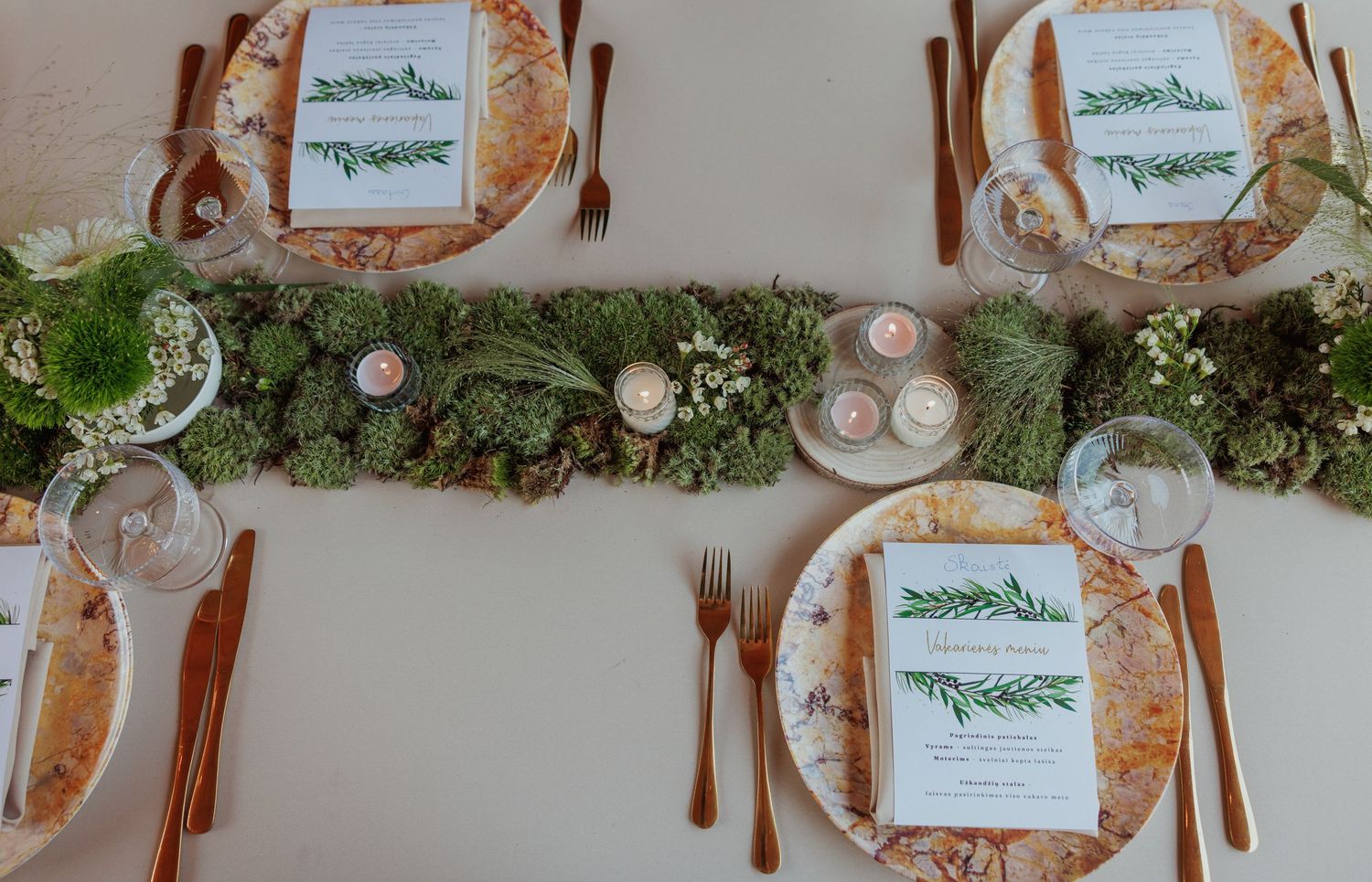 Wedding table decorated with moss runner, rosemary menu cards, and copper flatware.