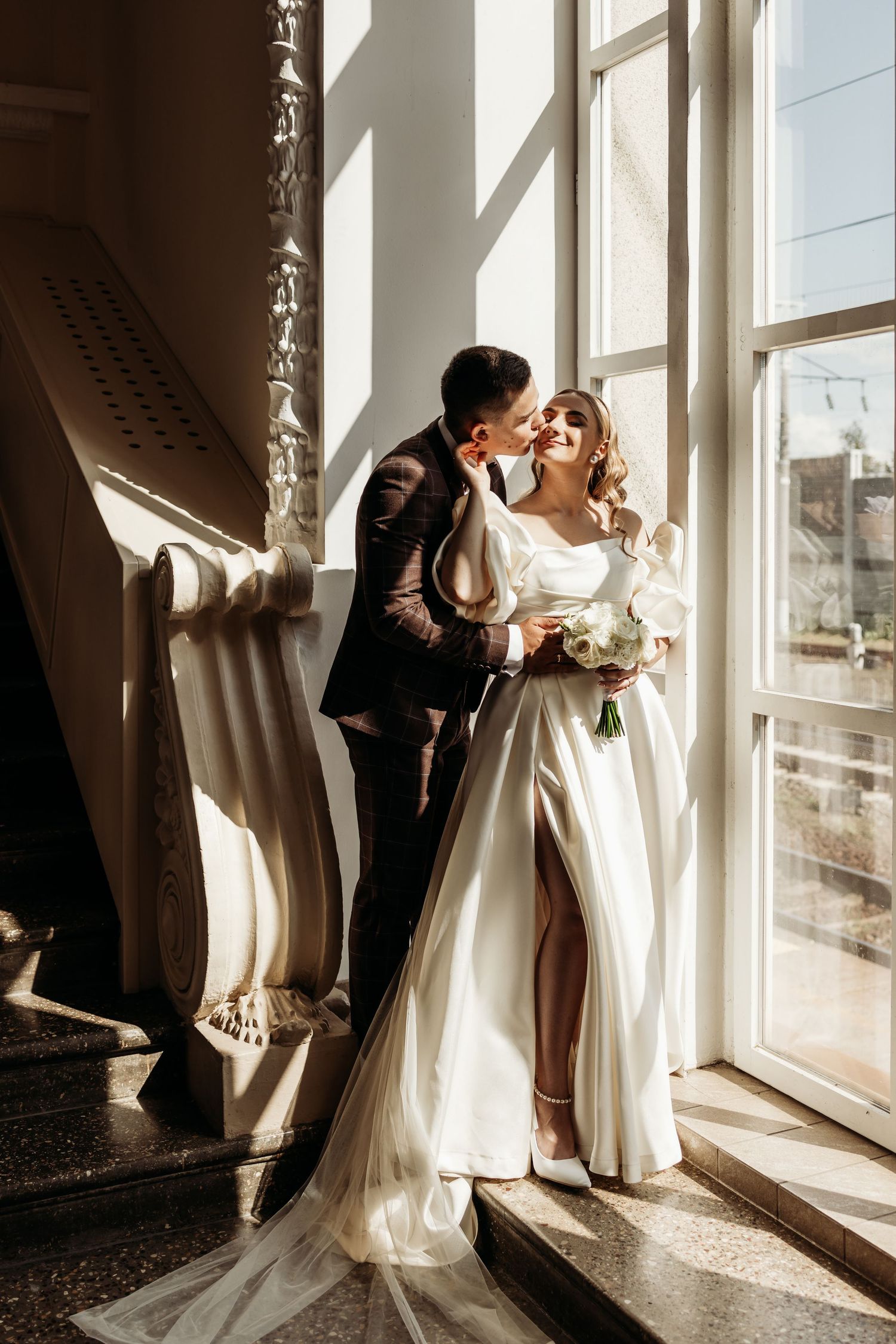 Romantic wedding photography silhouettes against large windows with natural sunlight streaming through.