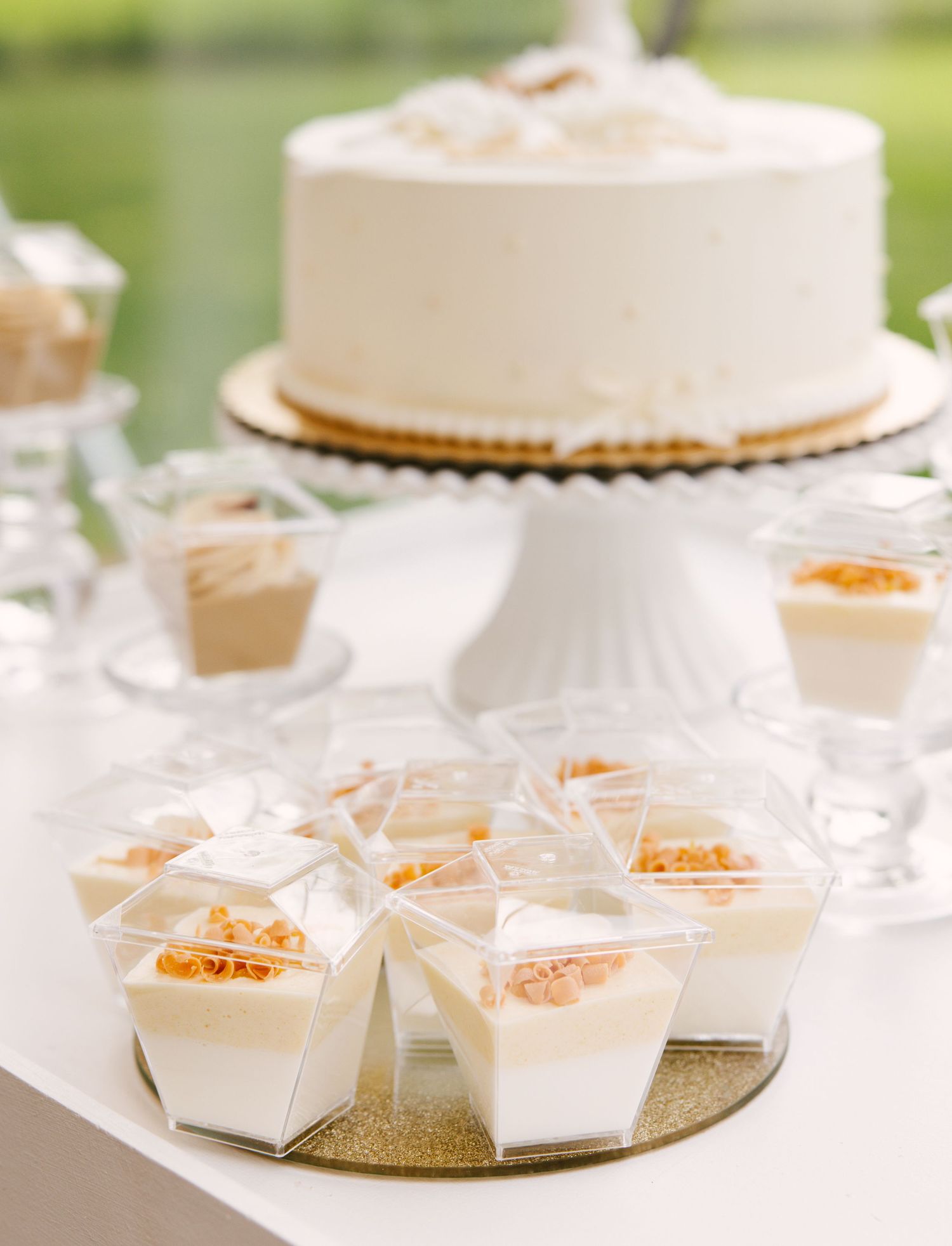 White wedding cake and individual dessert boxes displayed on glittery gold surface.