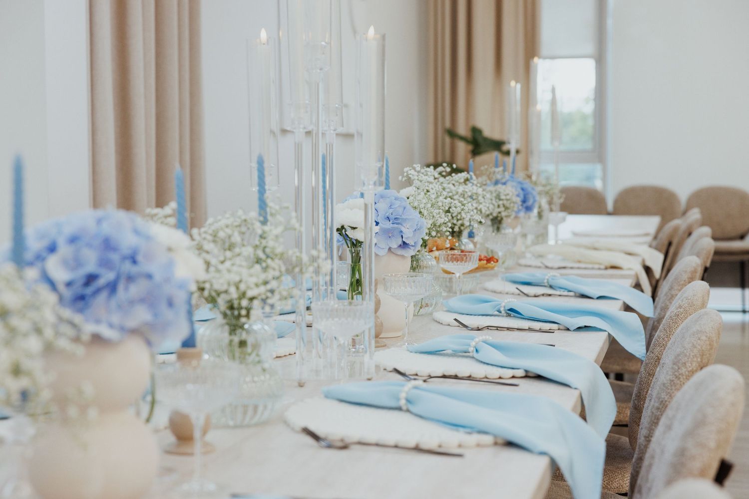 Long dining table set with blue and white decor, featuring elegant place settings and floral arrangements.