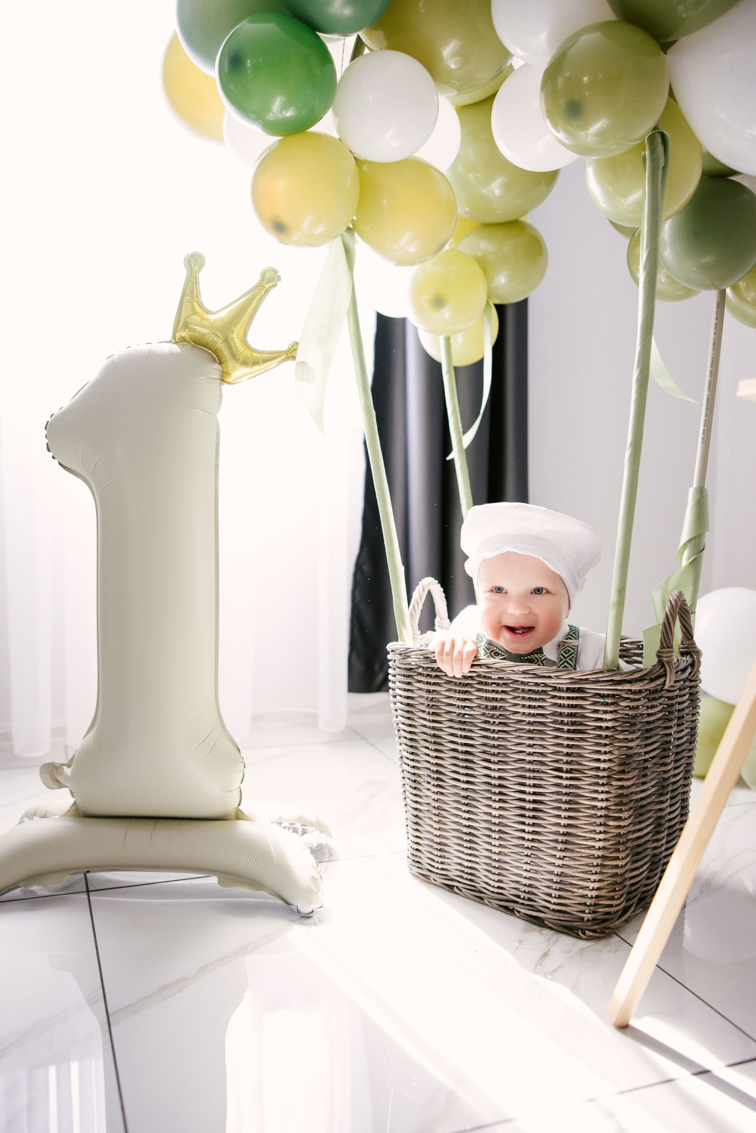 Whimsical hot air balloon themed party setup with green and white balloons floating above a wicker basket.