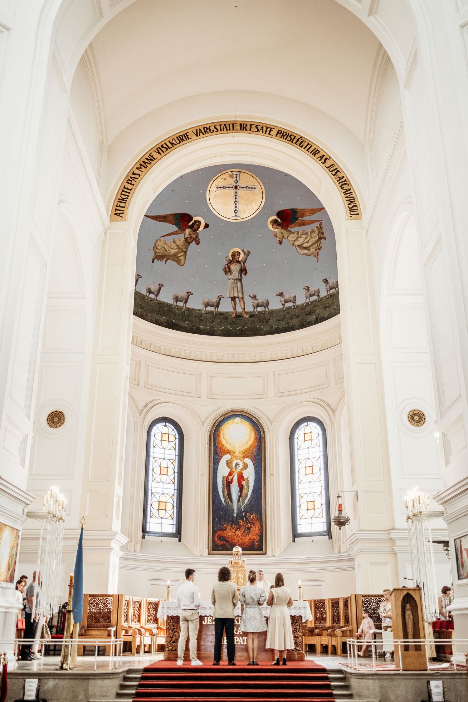 Interior of a white church sanctuary with arched ceilings, stained glass windows, and religious artwork in the altar area.