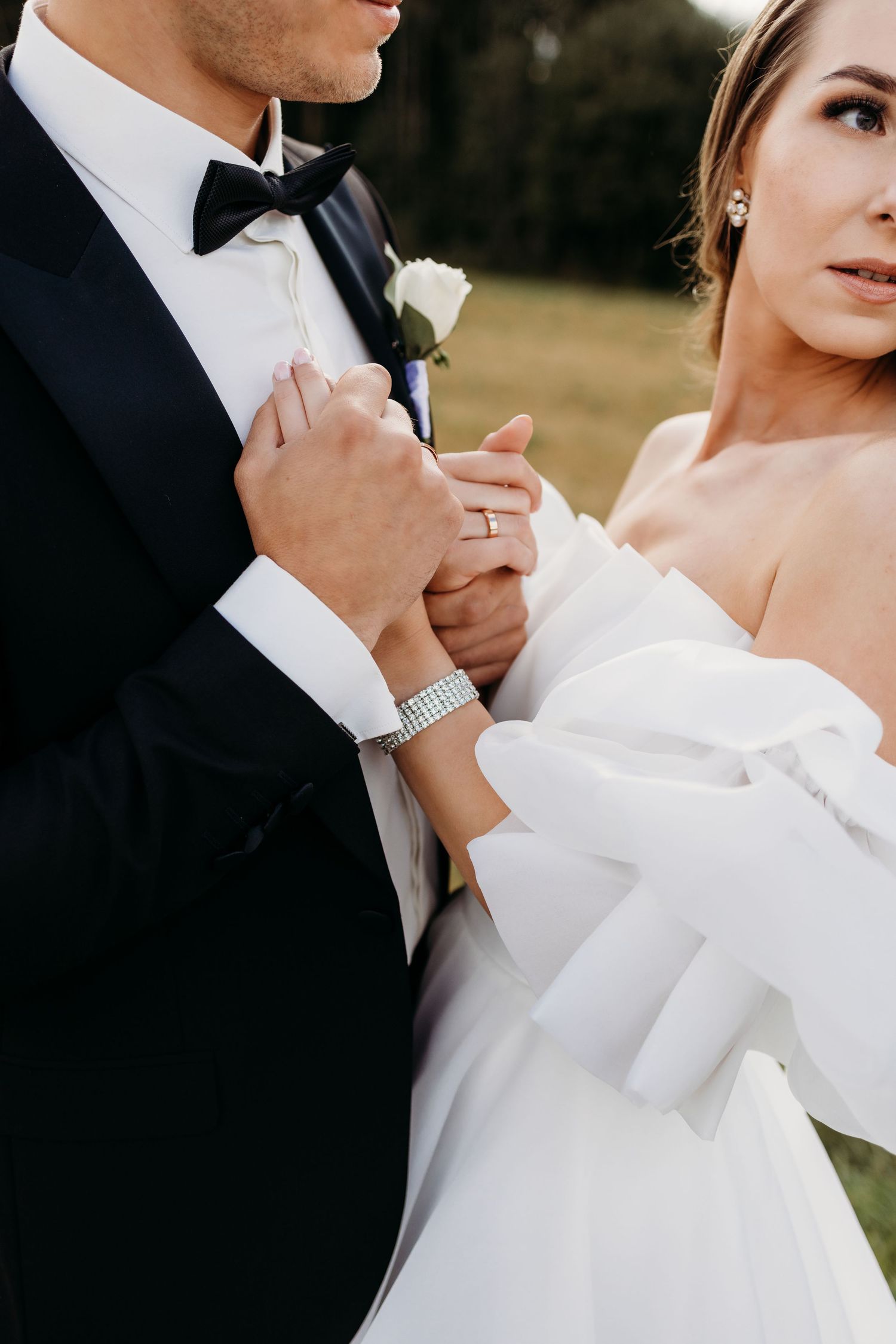 Close-up romantic wedding portrait showing elegant details of a bride's white dress and groom's formal attire.