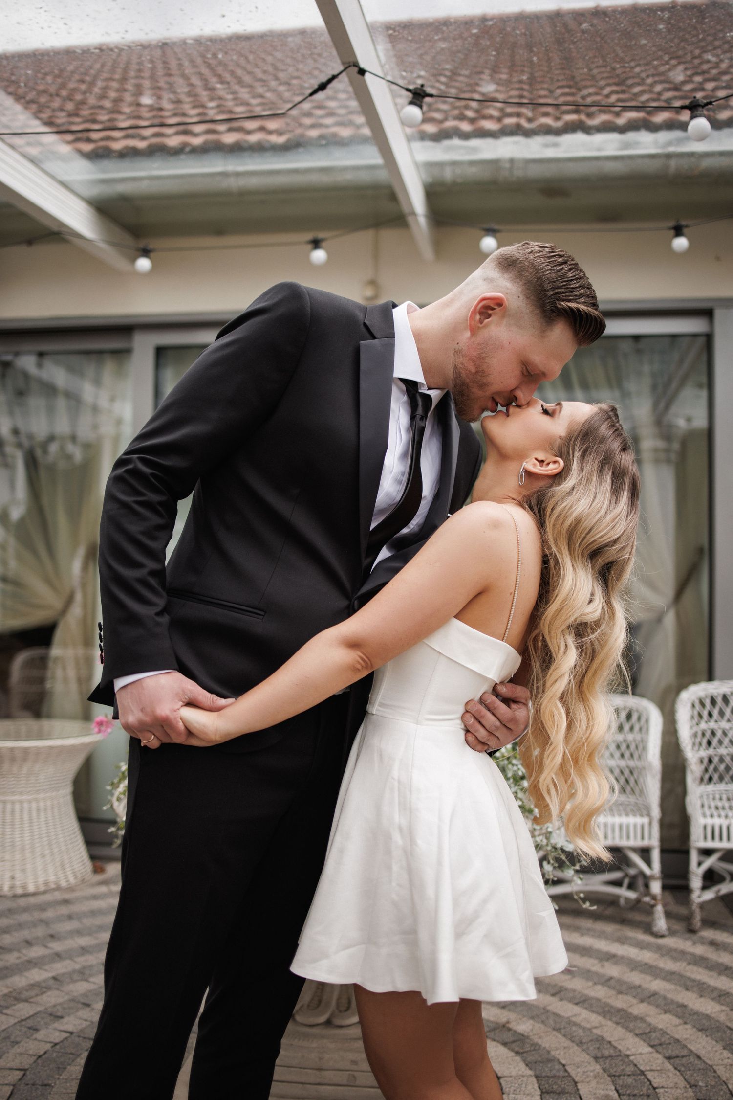 Intimate wedding couple sharing romantic moment on brick patio with white dress and black suit.