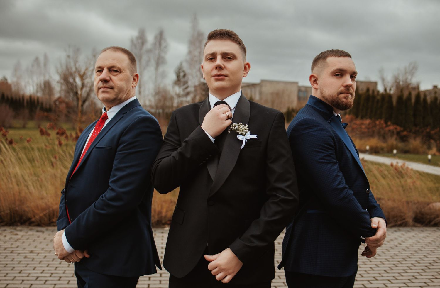 Groomsmen in navy suits lined up outdoors in dramatic panoramic shot.