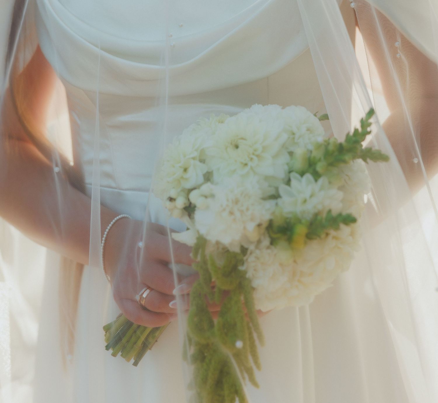 Close-up detail of white hydrangea wedding bouquet against bridal gown.
