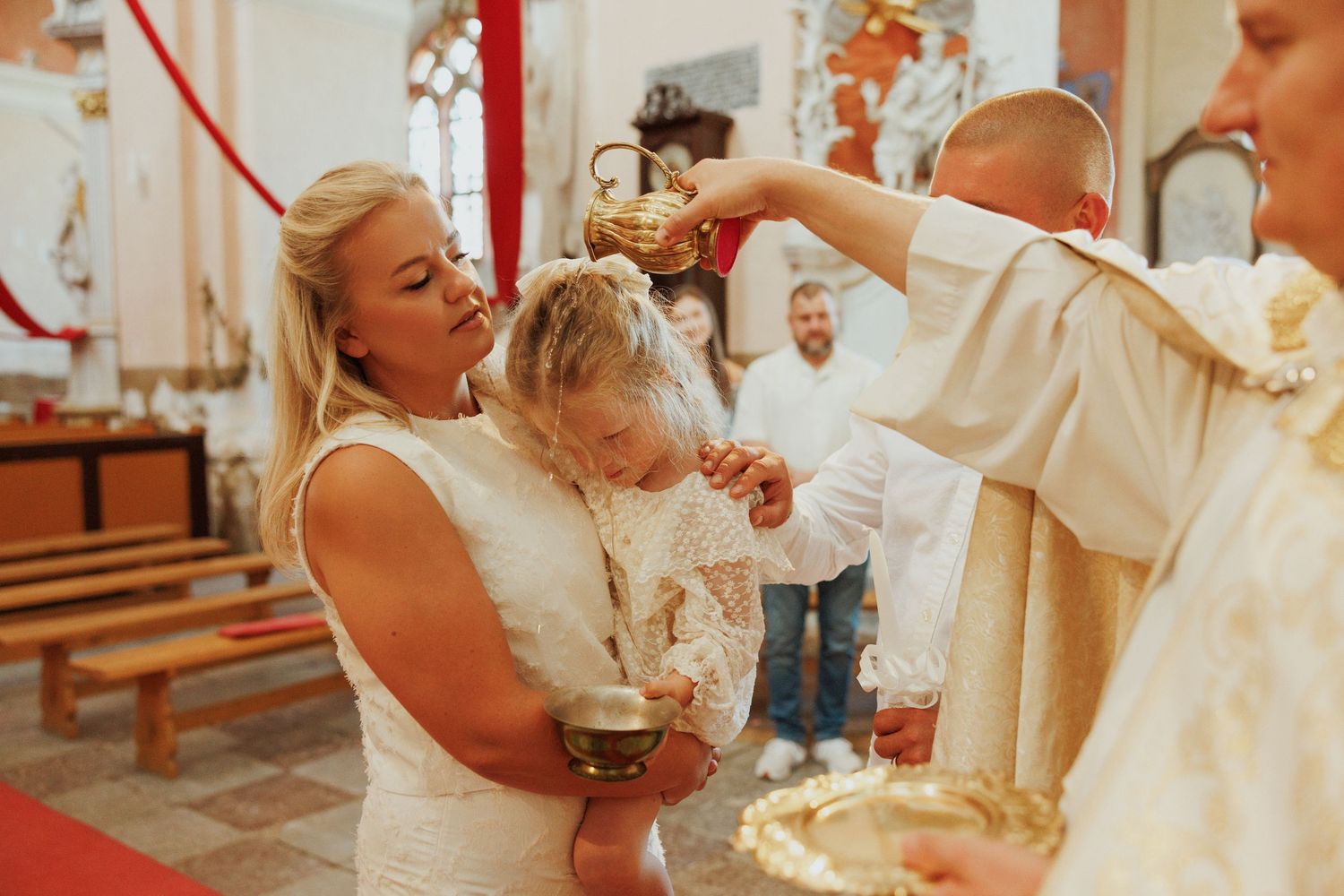A baptism ceremony takes place in a church as a priest performs the blessing ritual with holy water.