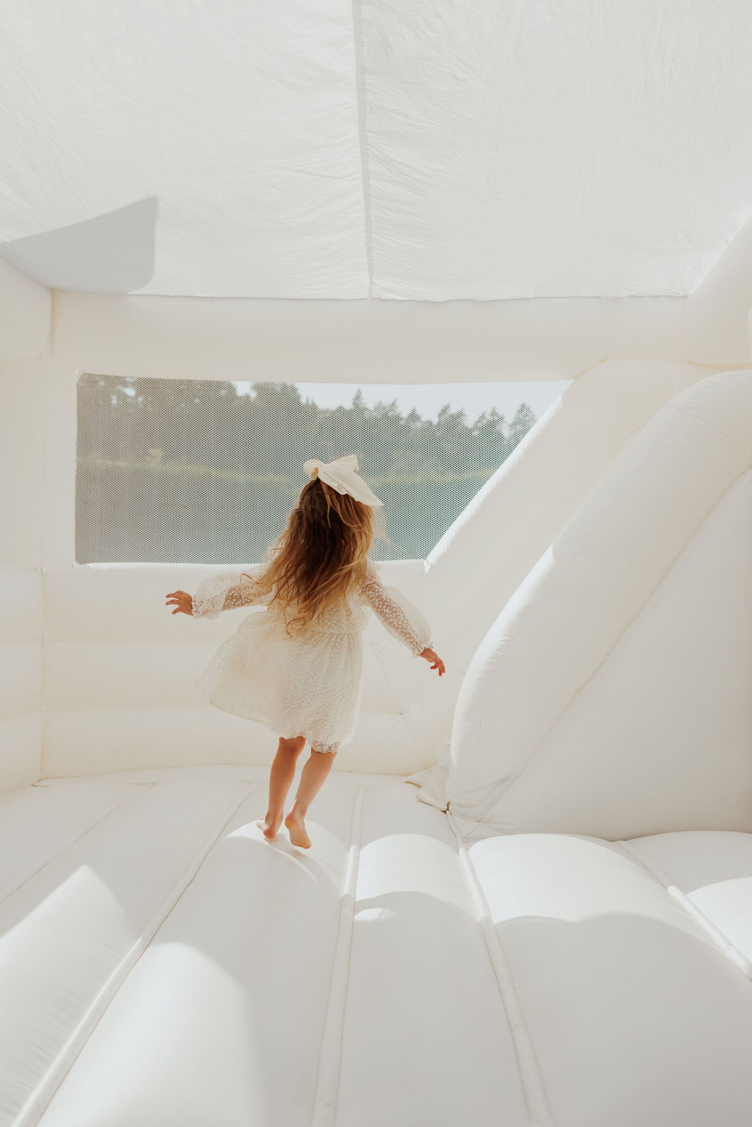 Child in white dress playing on ethereal white fabric backdrop creating dreamy atmosphere.