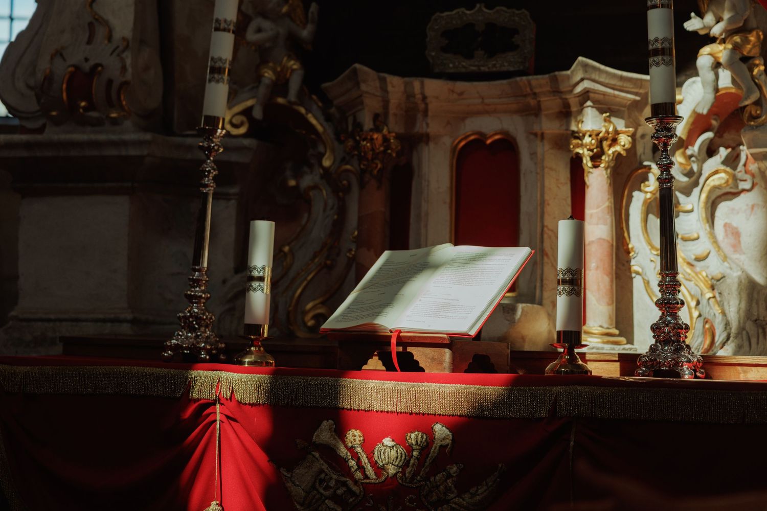An open religious book on a red-draped altar inside an ornate church with golden columns and decorative elements.