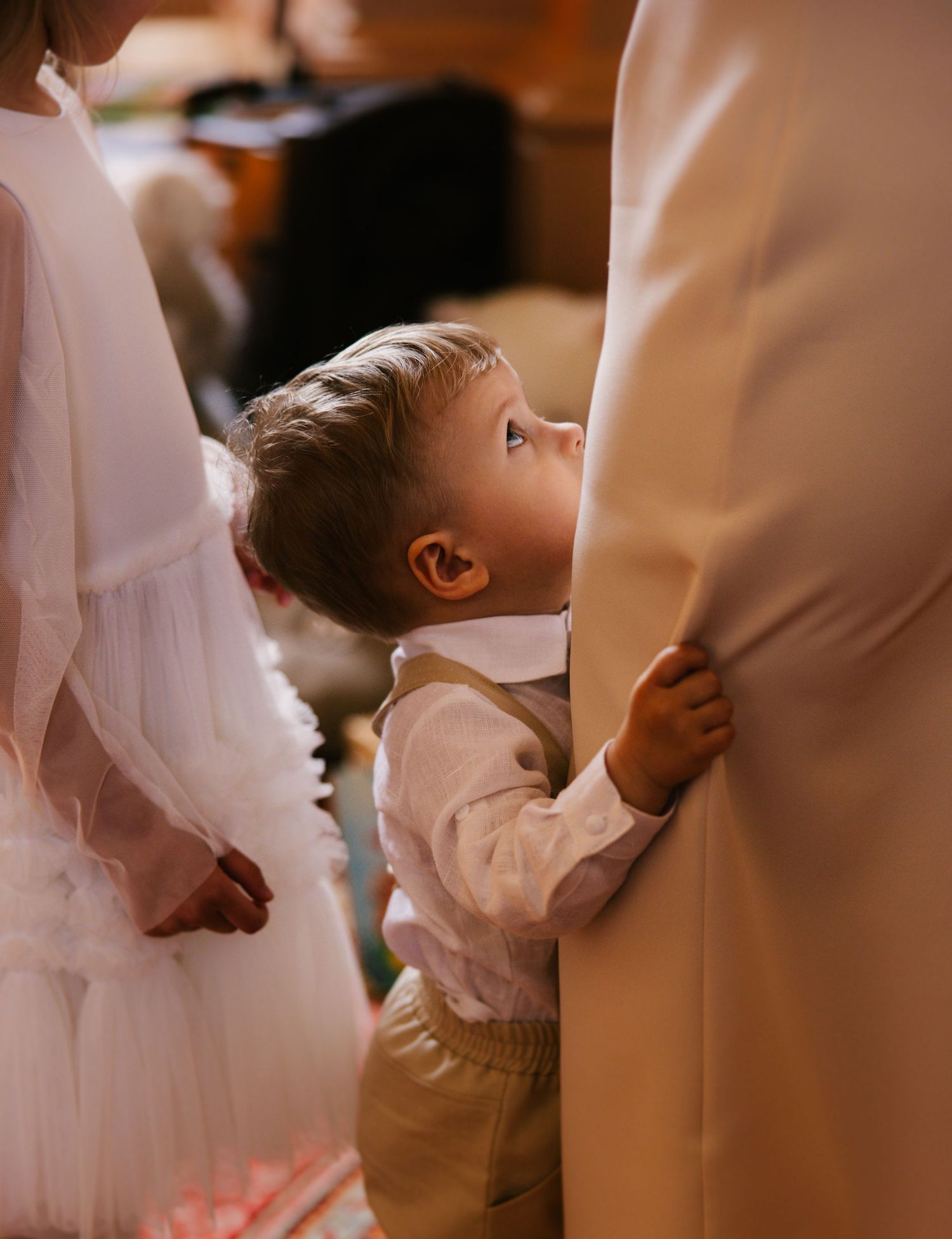 A young child in white clothing reaches up during what appears to be a wedding ceremony or formal event.