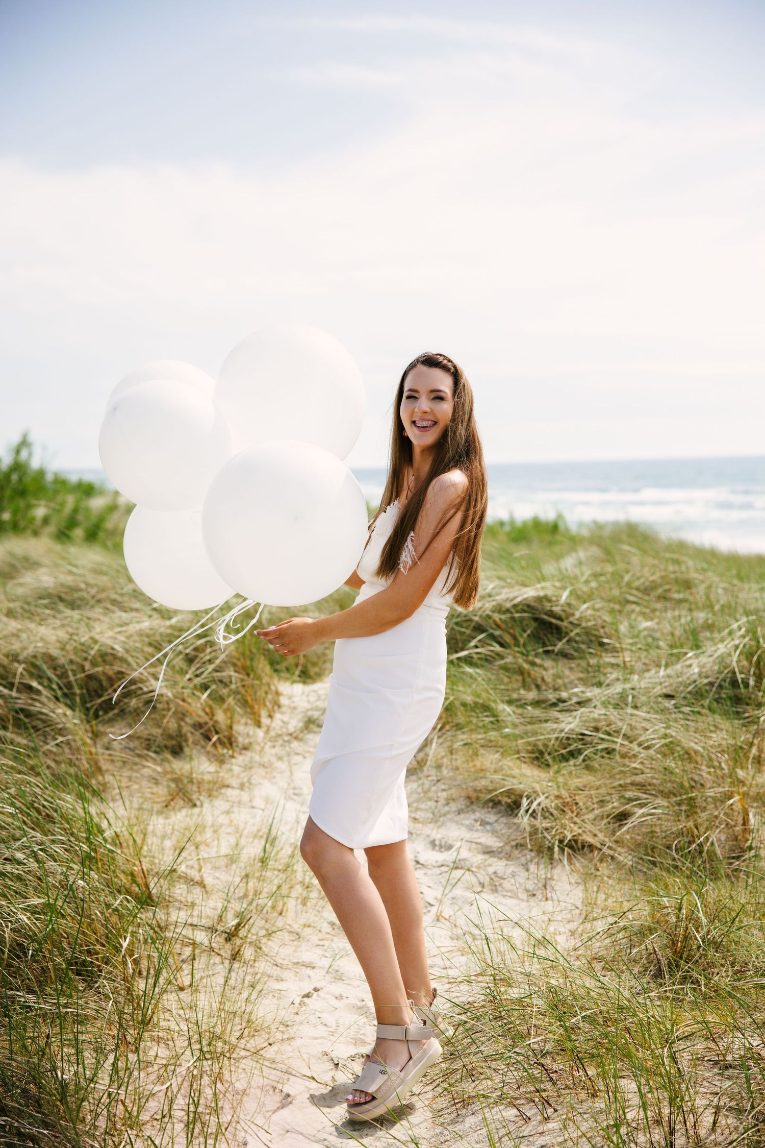 Beachy photoshoot scene with white balloons among coastal dunes and grass.