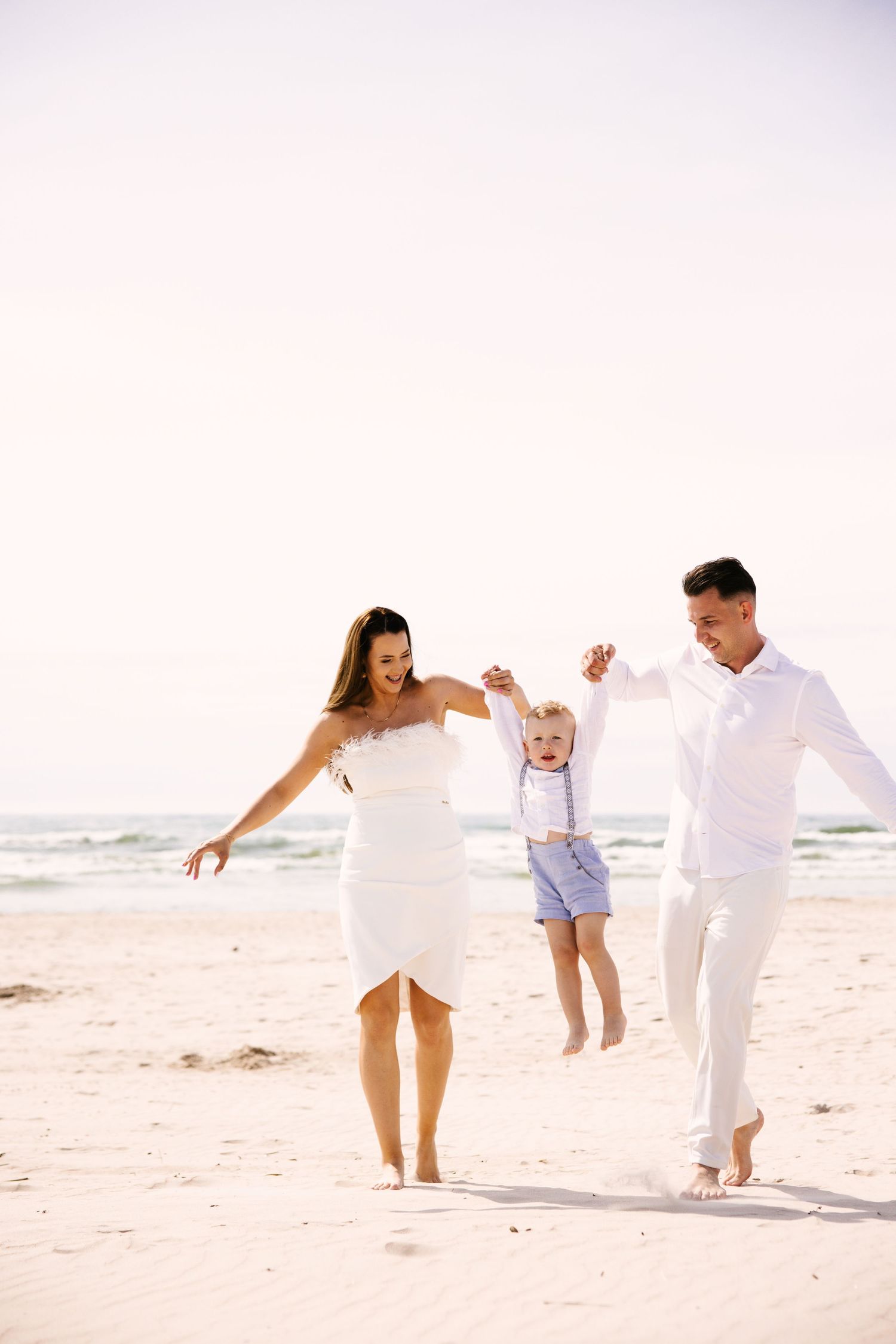 A joyful family plays together on a pristine white sand beach at sunset.