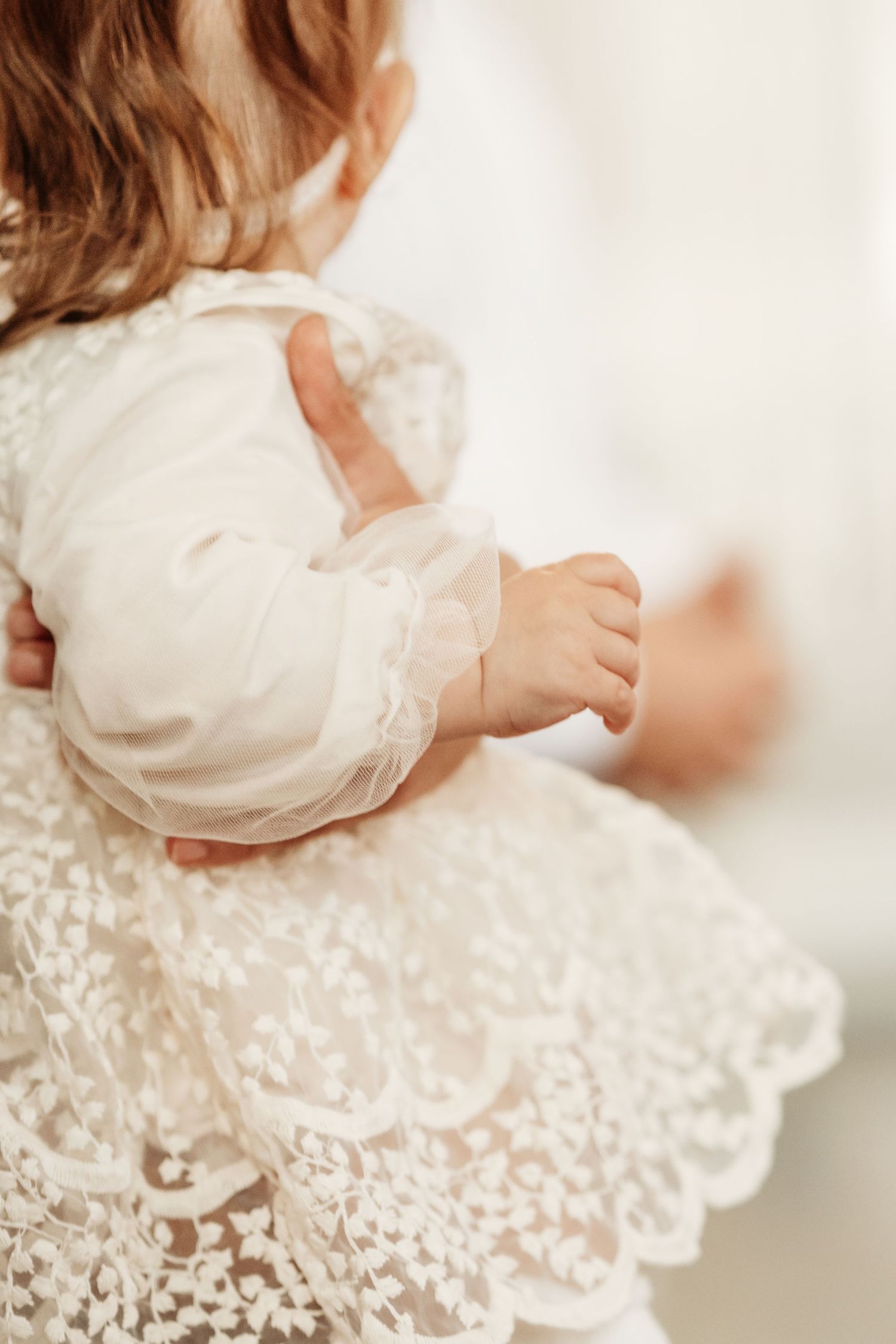 Close-up details of delicate white lace and ruffles on a baby's christening gown in soft natural light.