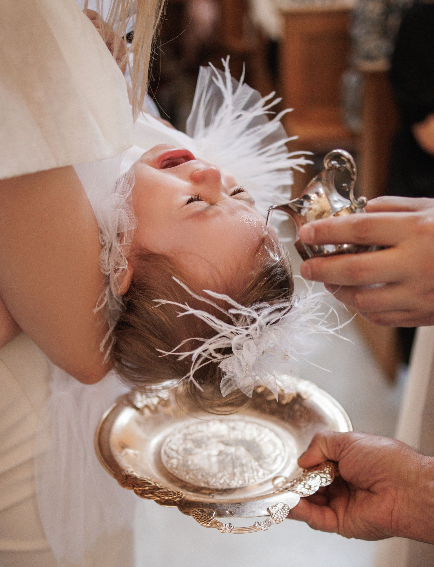 A person in white lies back on a silver platter while someone pours liquid during what appears to be a ceremonial moment.