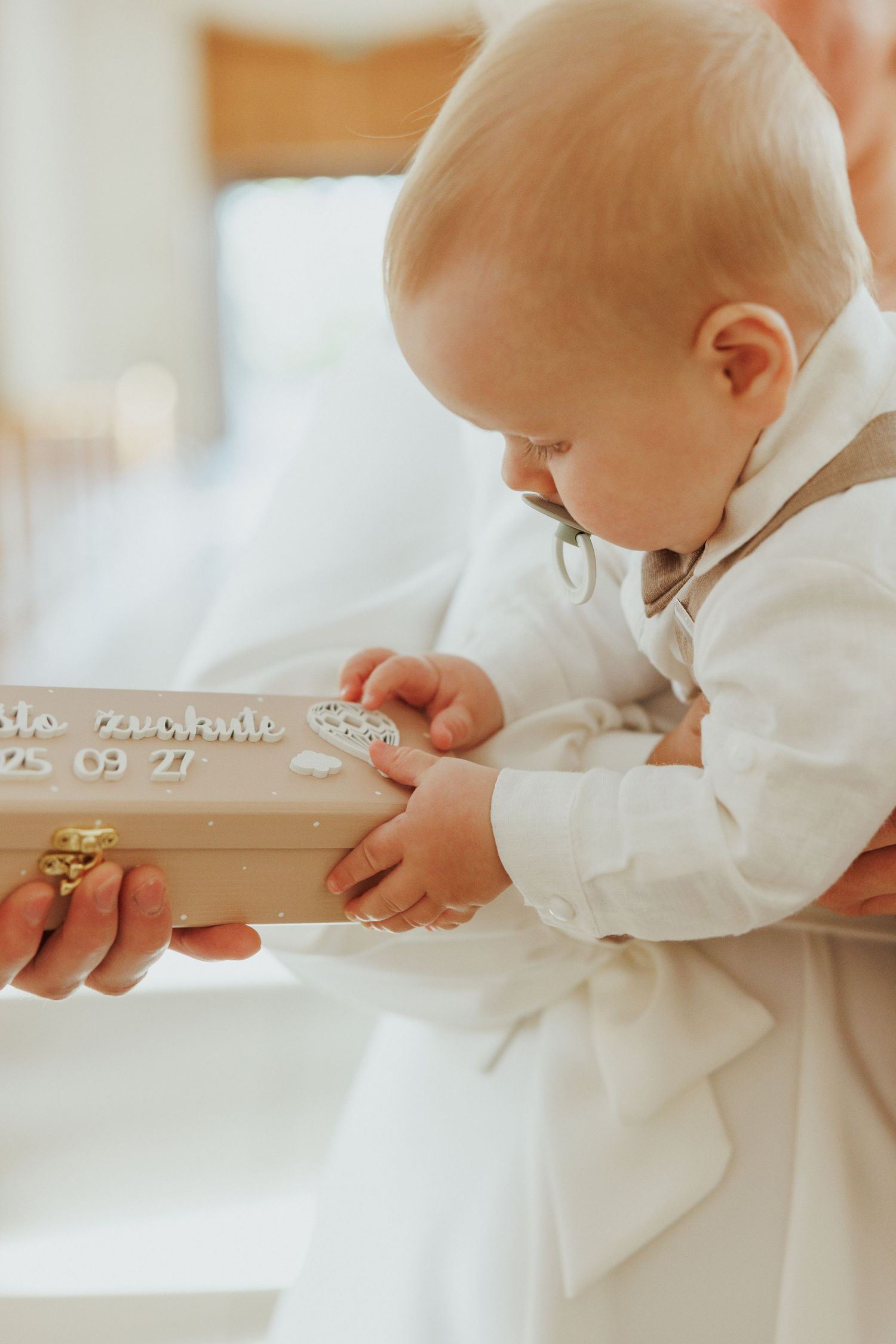 Baby in white baptismal gown holds a delicate cross necklace during a christening ceremony.