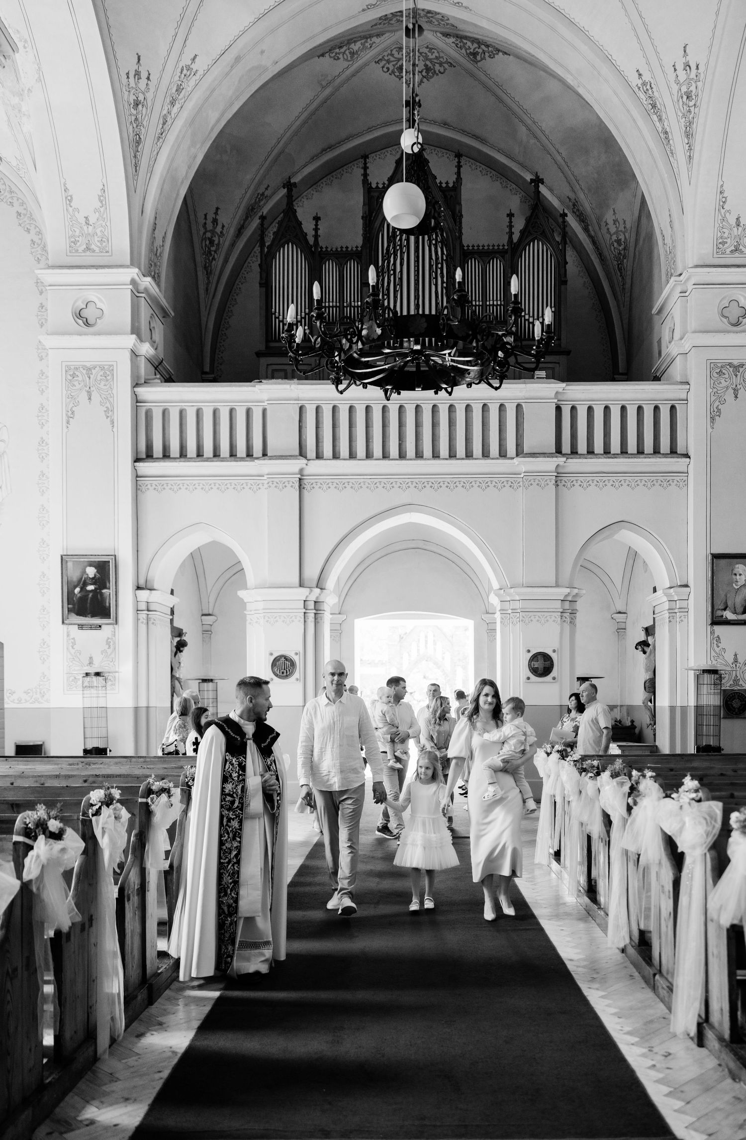 Black and white photograph of a grand church interior with arched ceilings and guests in white attire.