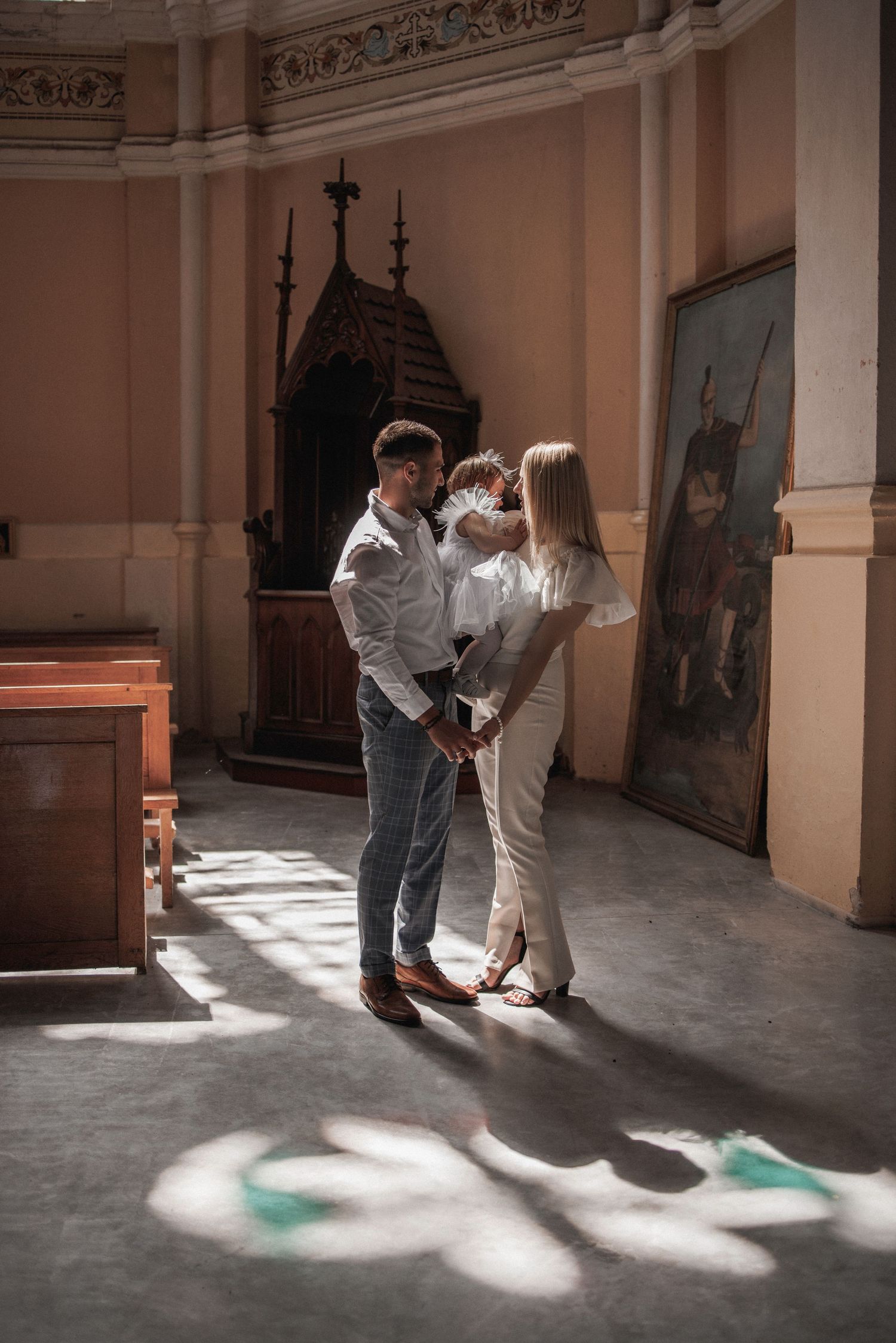 Dancing figures cast shadows on a church floor as sunlight streams through stained glass windows.